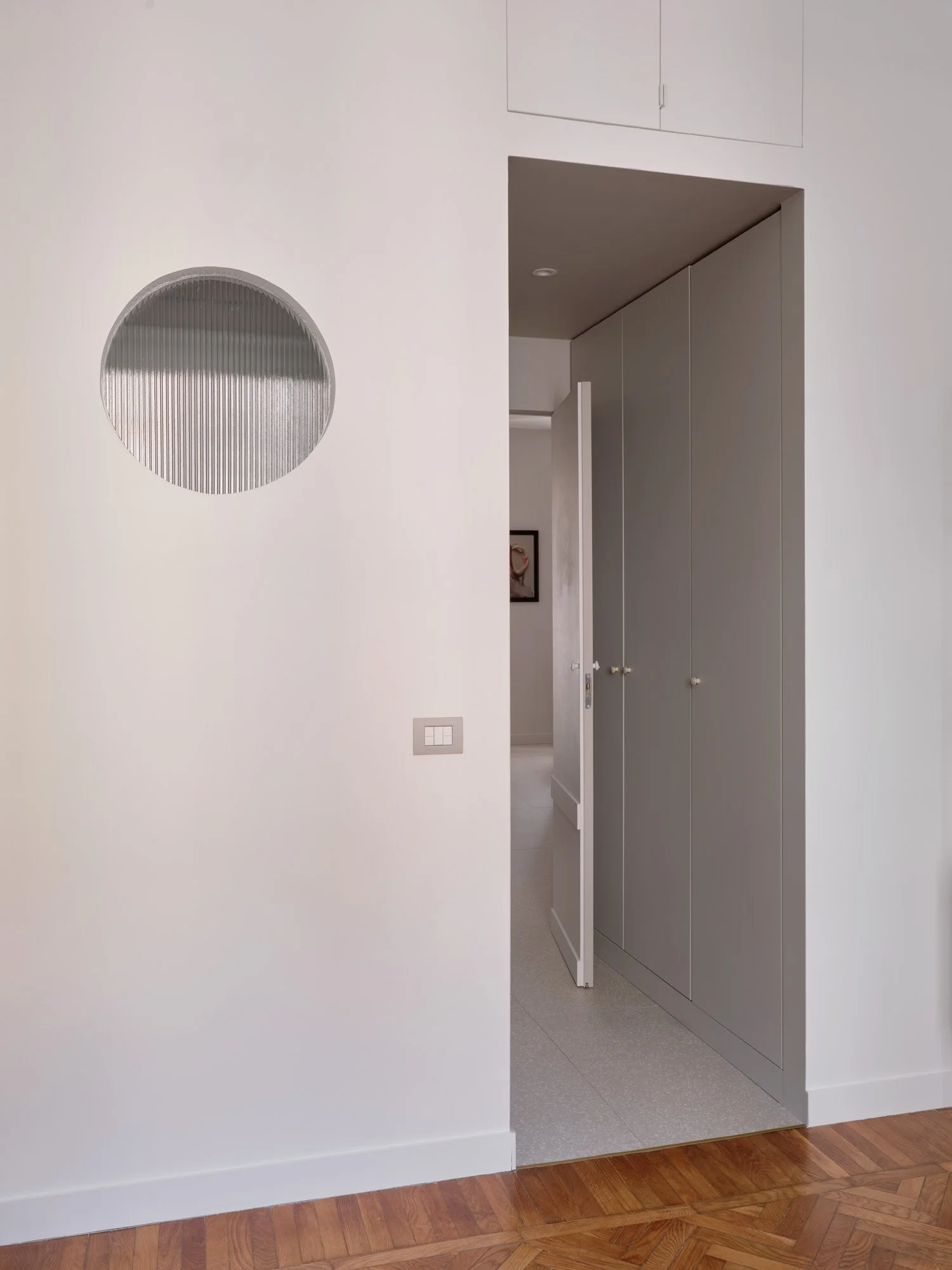 Ingresso di una casa con pareti bianche, porta apribile e armadi gray, pavimento in parquet.