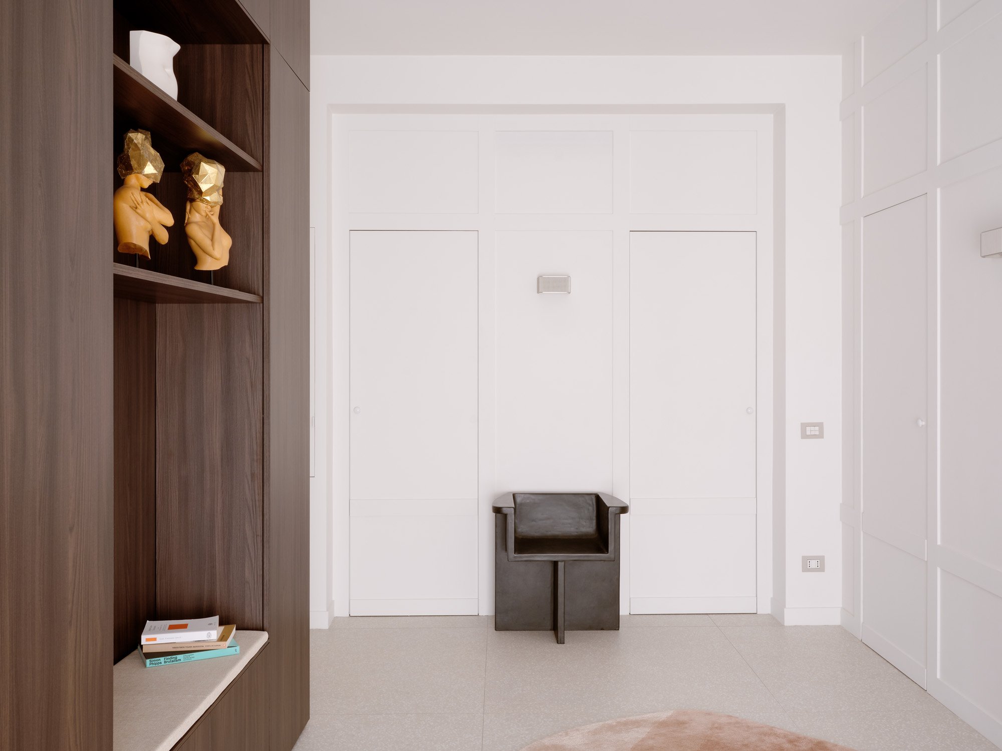 Interno moderno con pareti bianche e armadi, una sedia nera e scaffali con statuette e libri.