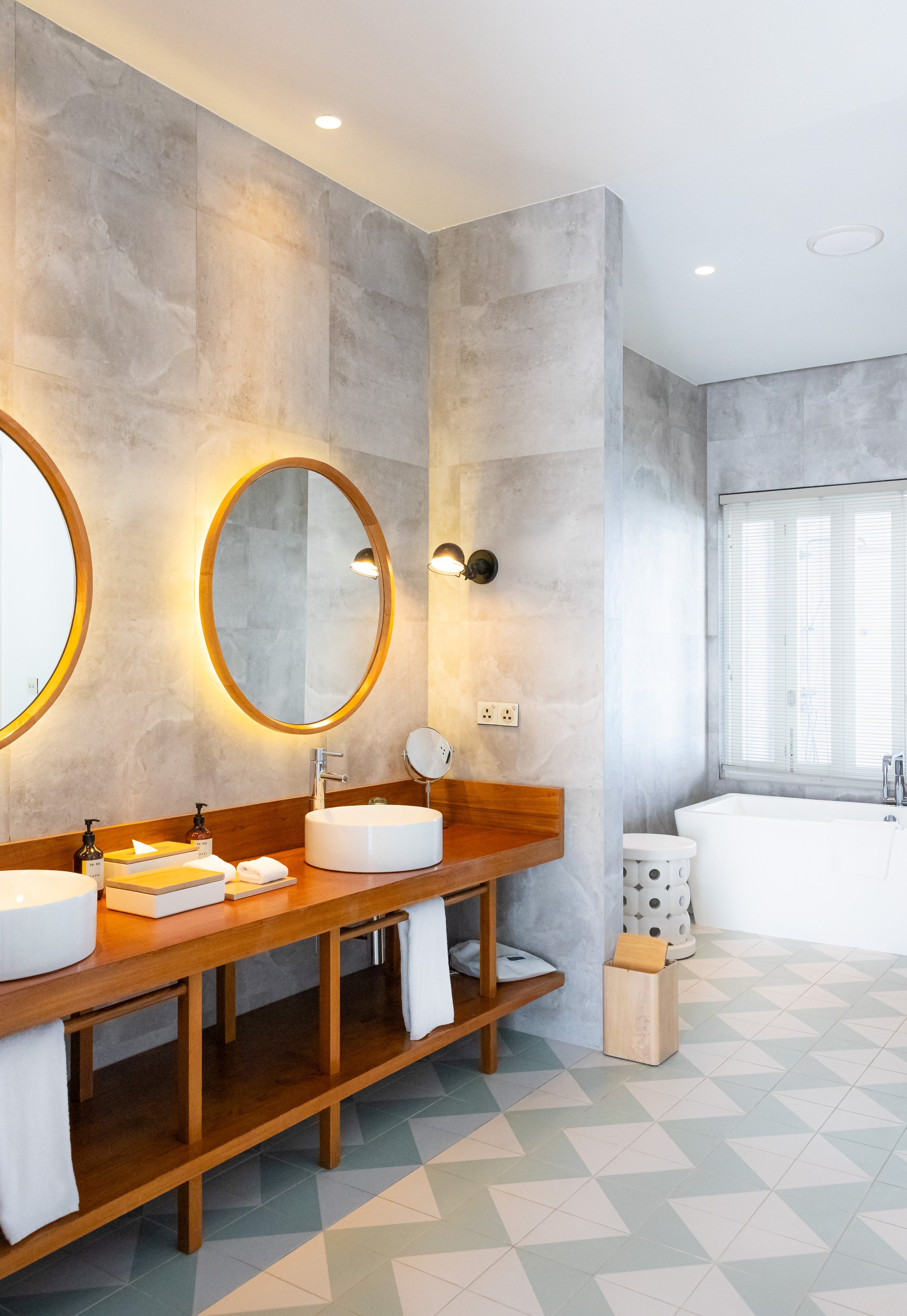 Modernes Badezimmer mit rundem Spiegel, Holzelementen und gemustertem Boden.