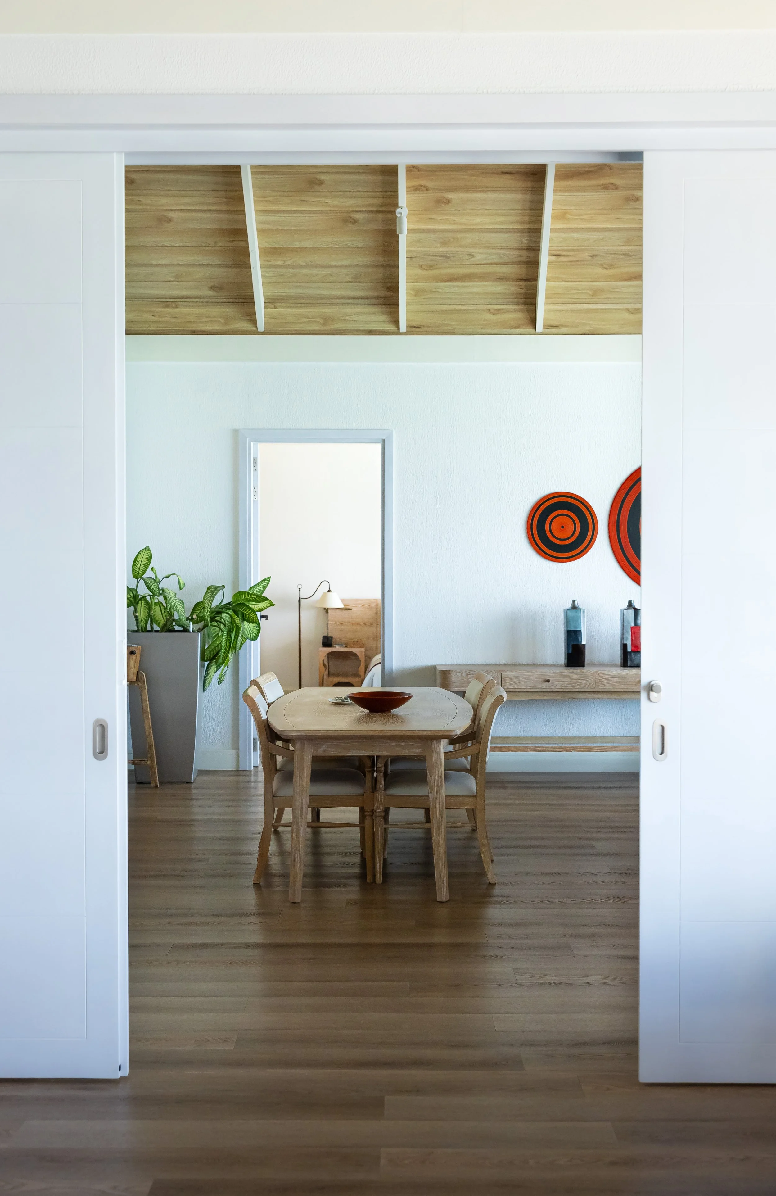 Wohnzimmer mit Tisch, braunem Parkettboden, schlichte Einrichtung.