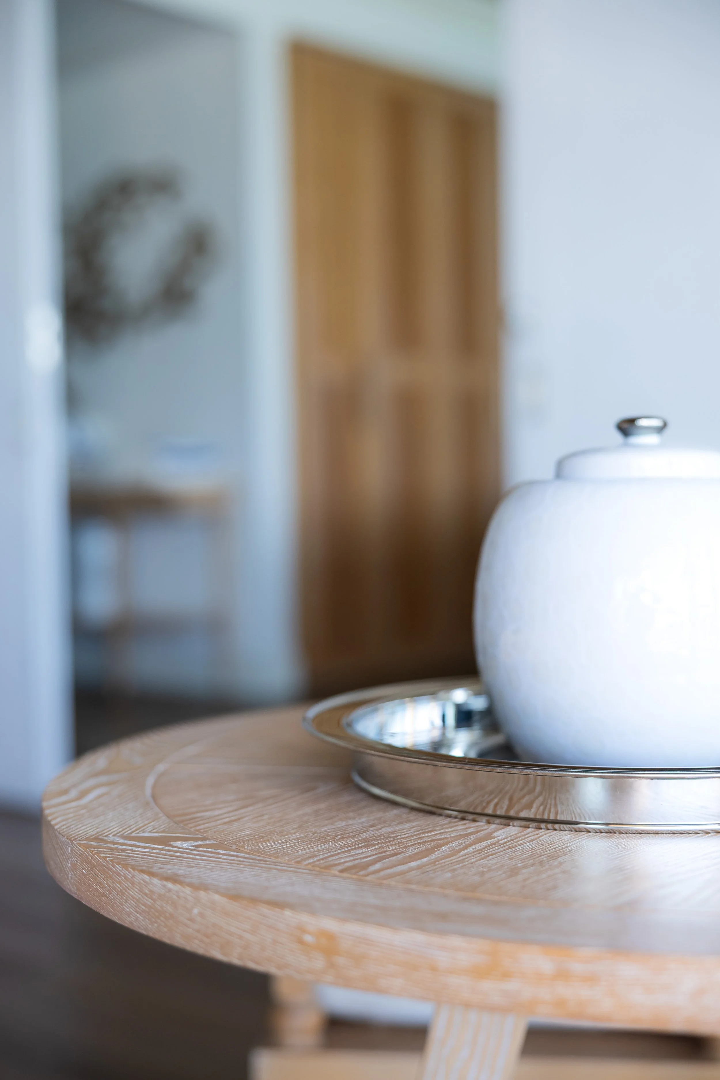 Detailaufnahme einer weissen runden Wase auf einem Holztisch im Wohnzimmer.