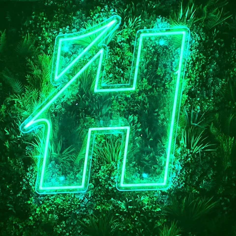 Green neon lightning bolt sign mounted on a leafy green wall.
