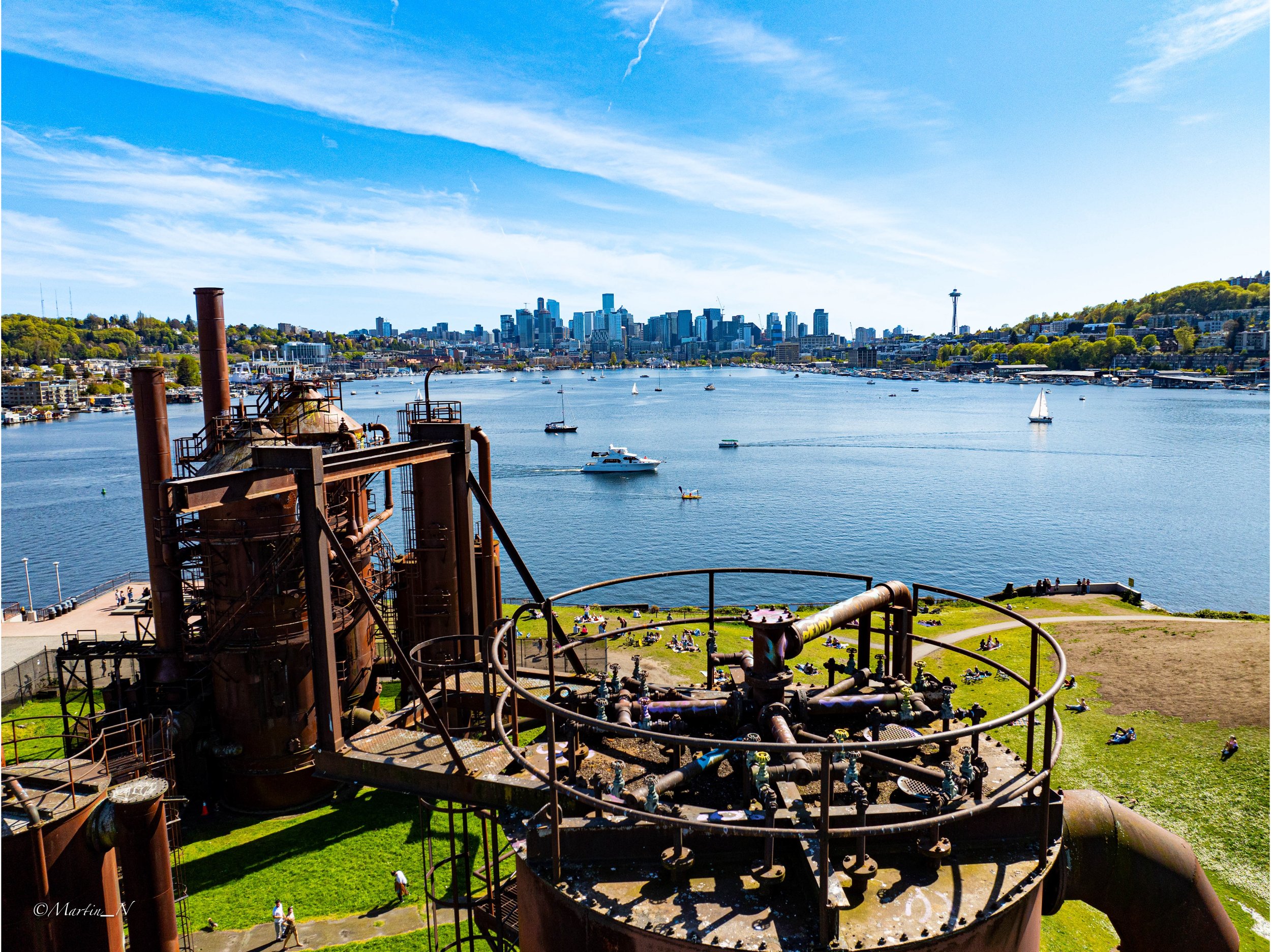View of city skyline across water, with boats sailing, and an industrial metal structure in the foreground.