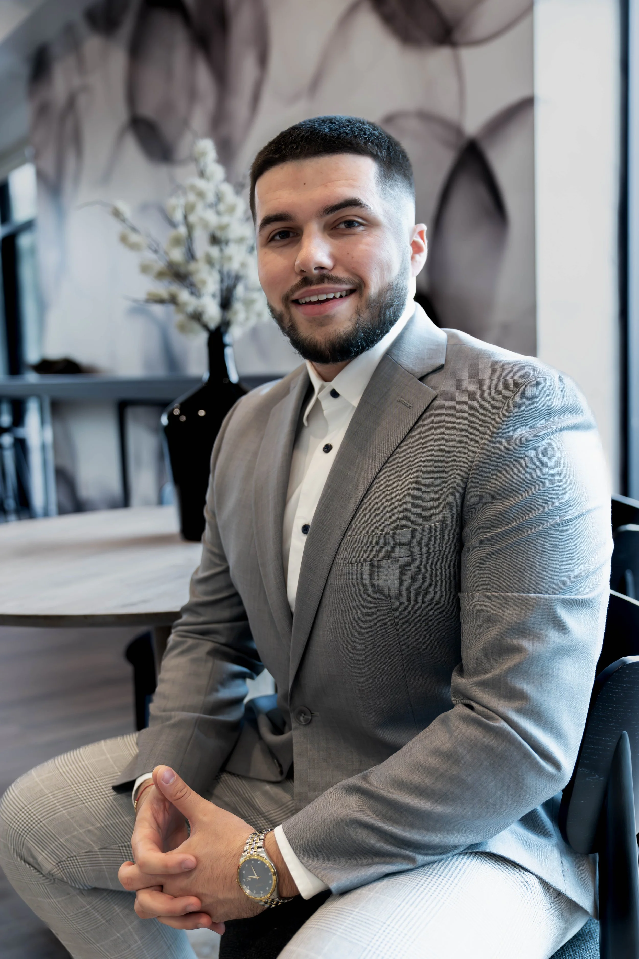 Man in gray suit sitting indoors, smiling