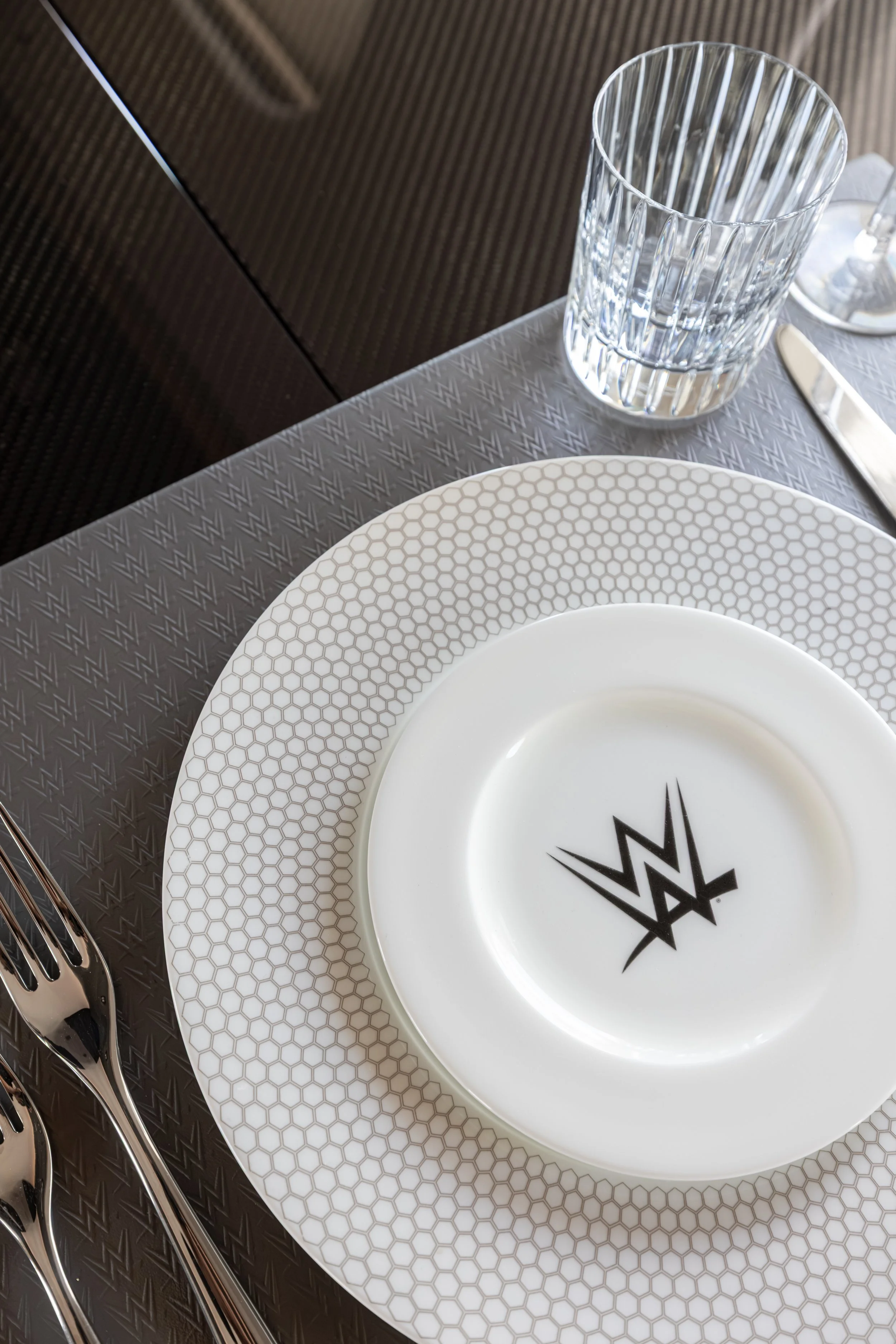 Empty glass on a table with WWE logo on plate, silverware on the side, and a textured table surface.