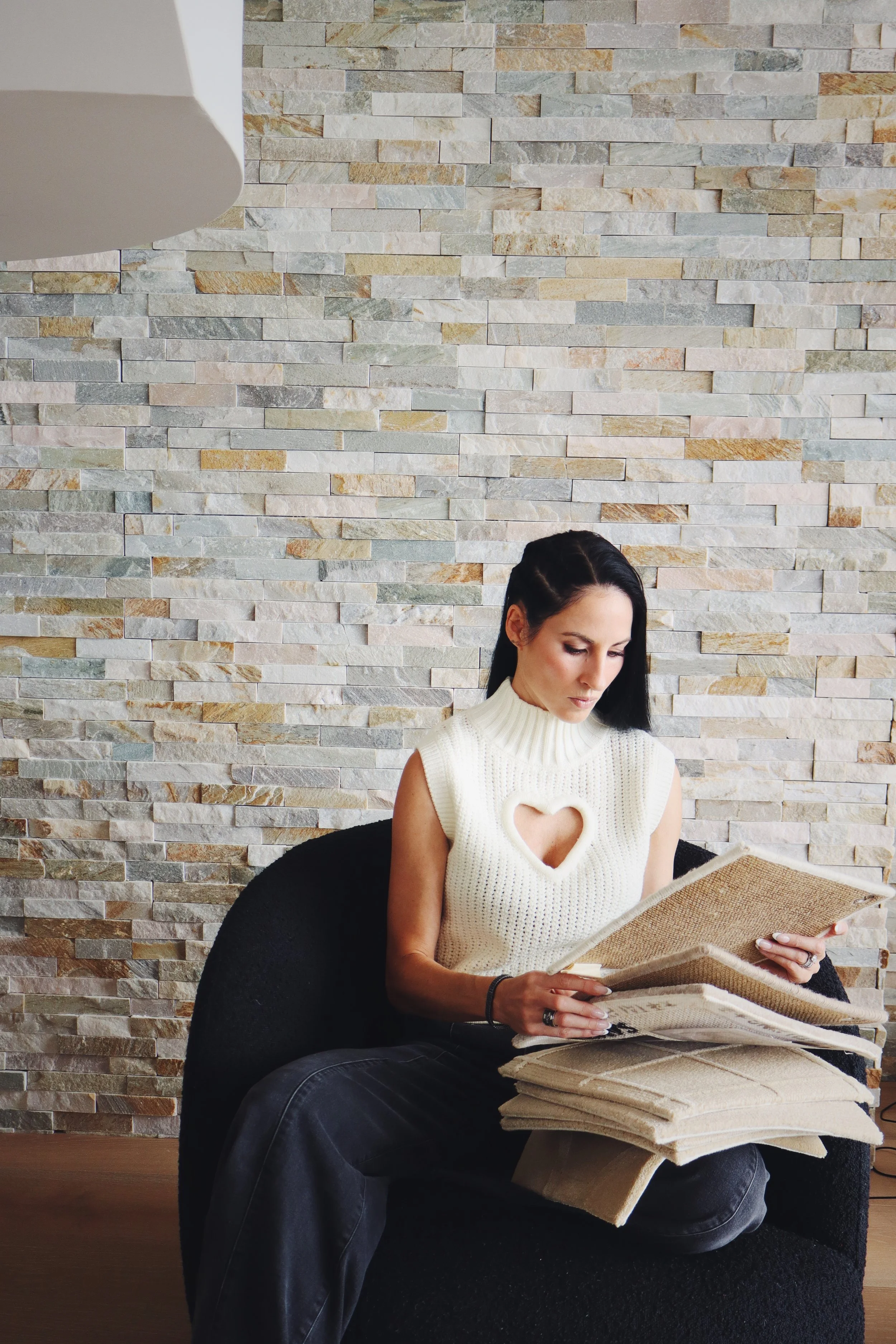 Top private jet designer Sarah Larranaga, wearing a sleeveless cream-knit sweater with a heart-shaped cutout, seated on a black chair, looking at a large open photo album.