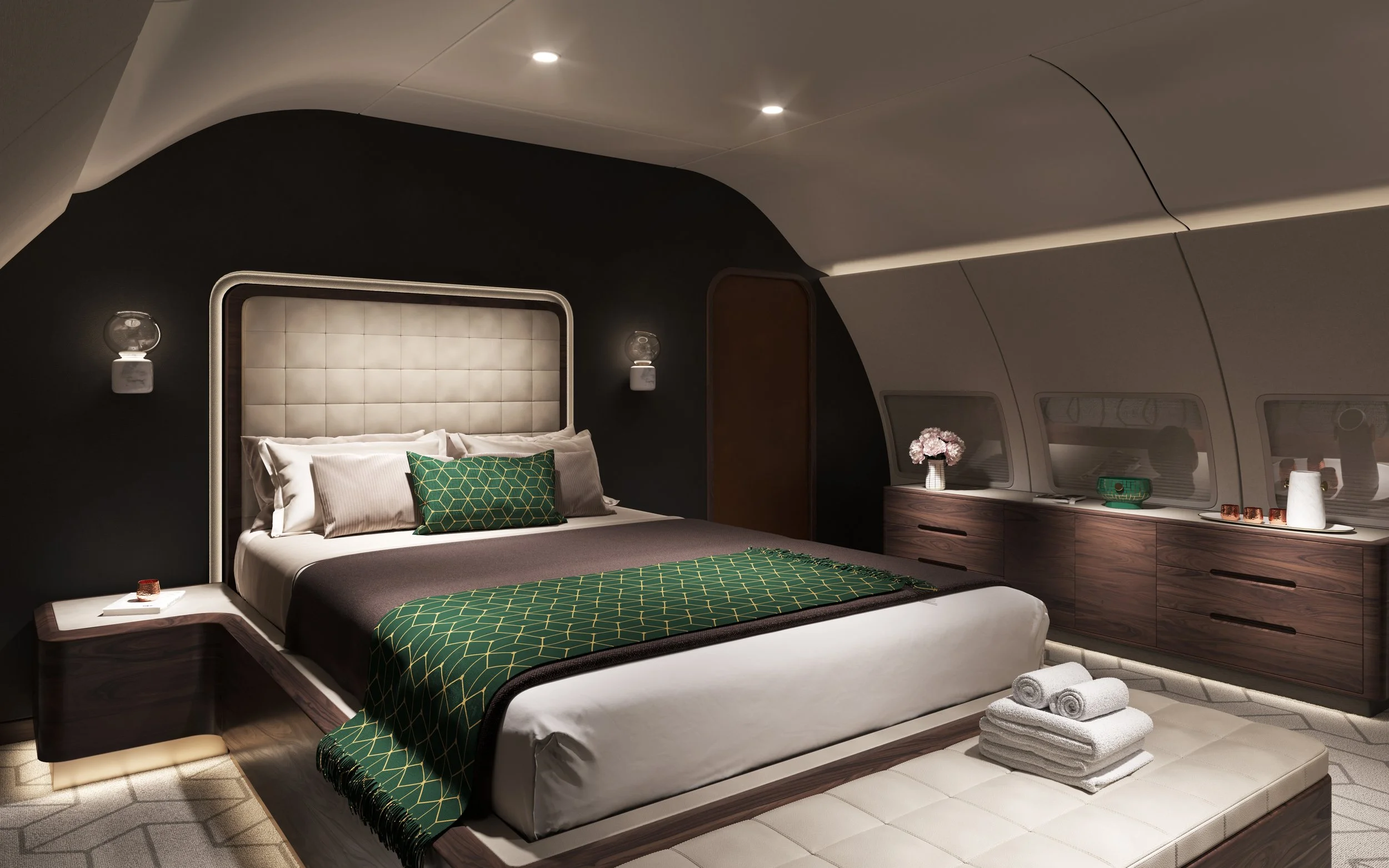 Luxurious bedroom designed by Sarah Larranaga, with a large bed, green patterned throw blanket, and matching pillows, set in an elegant space with dark and light wood furnishings and decorative accents, including flowers and candles.