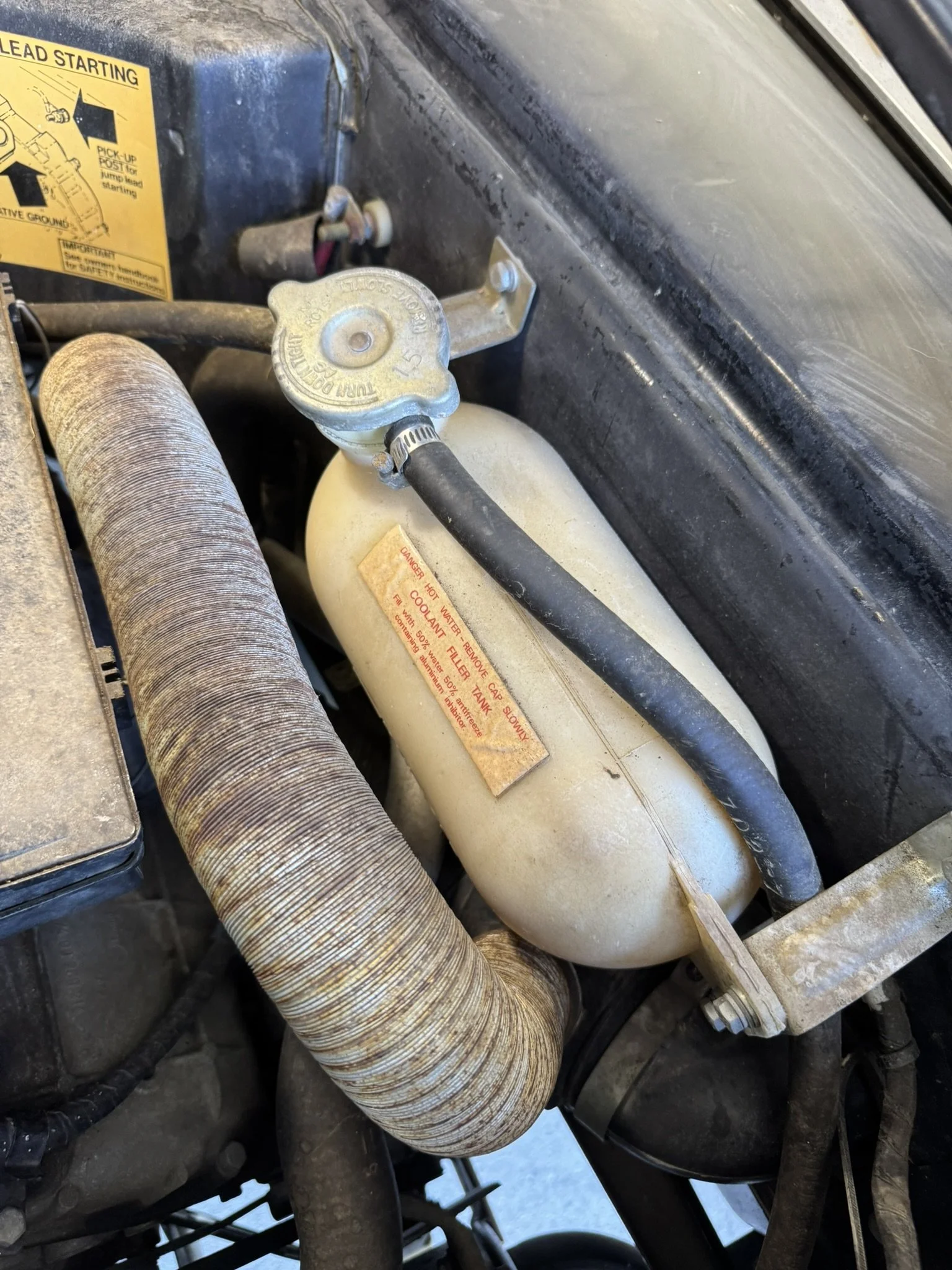Original plastic coolant overflow bottle. These have a tendency to crack with age, so I replaced mine with a modern stainless steel version.
