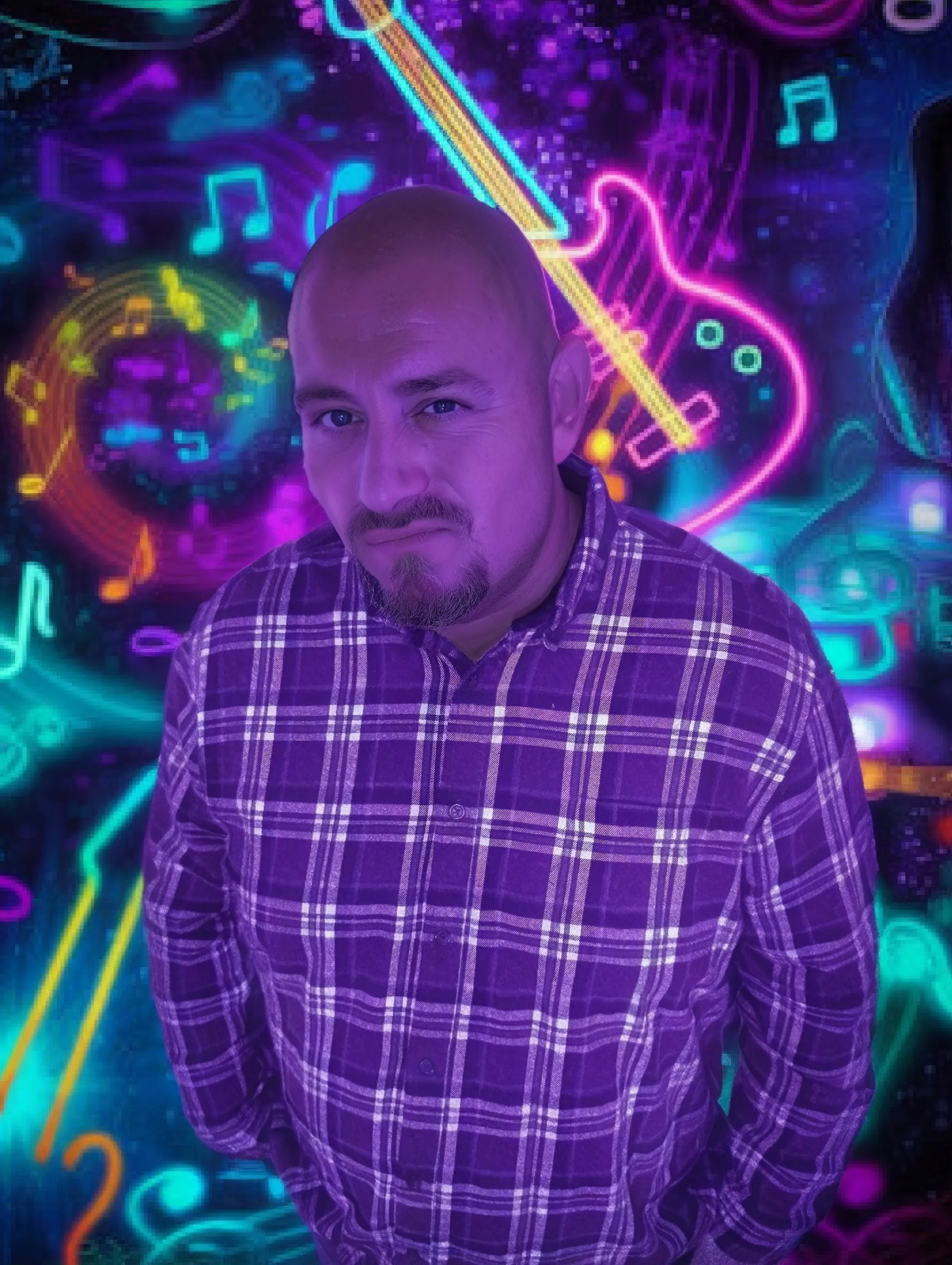 A man with a shaved head, goatee, and wearing a plaid shirt is standing in front of a colorful neon music-themed background.