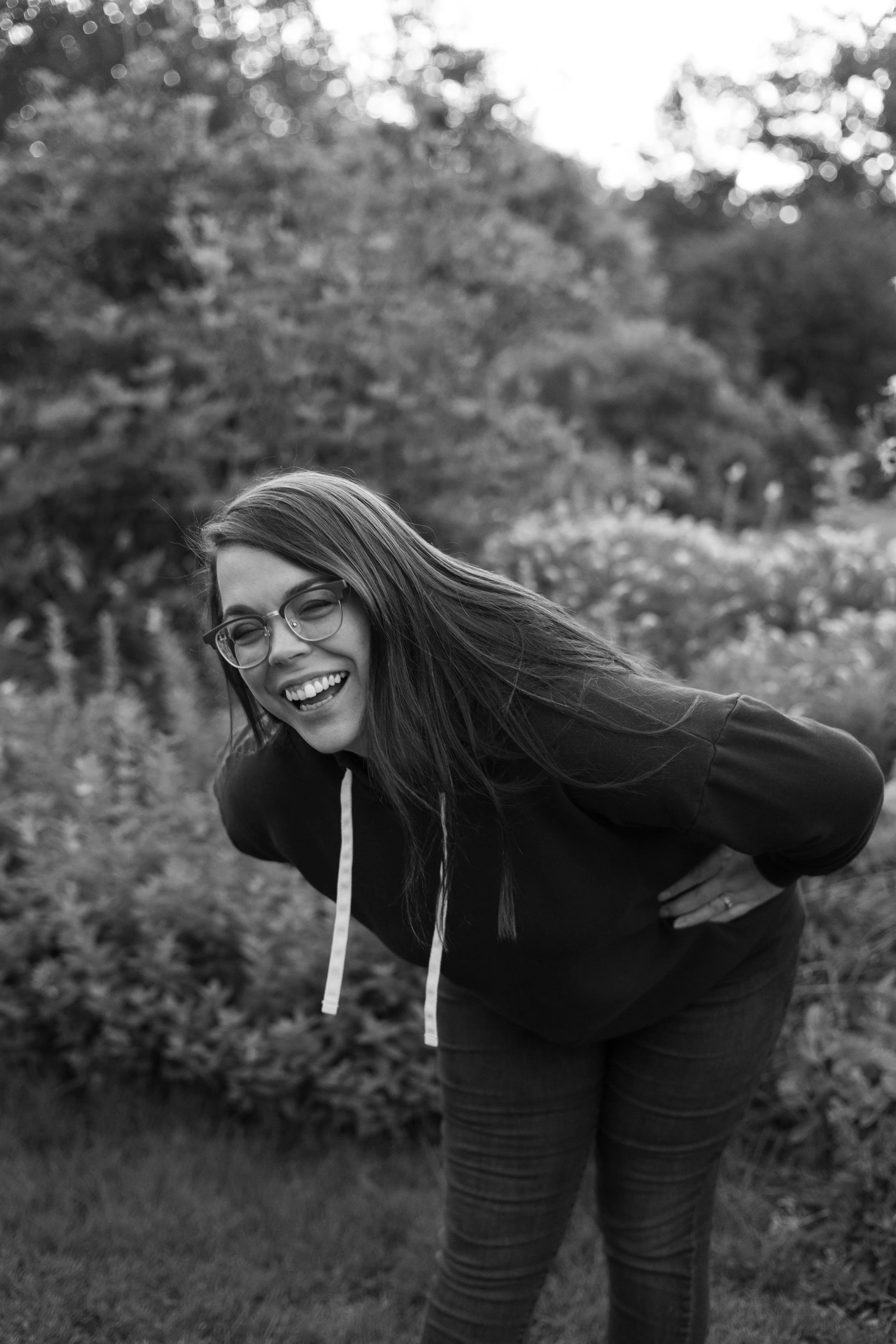 Photo of woman standing, bent over at the waist and laughing, smiling, with her hands on her hips