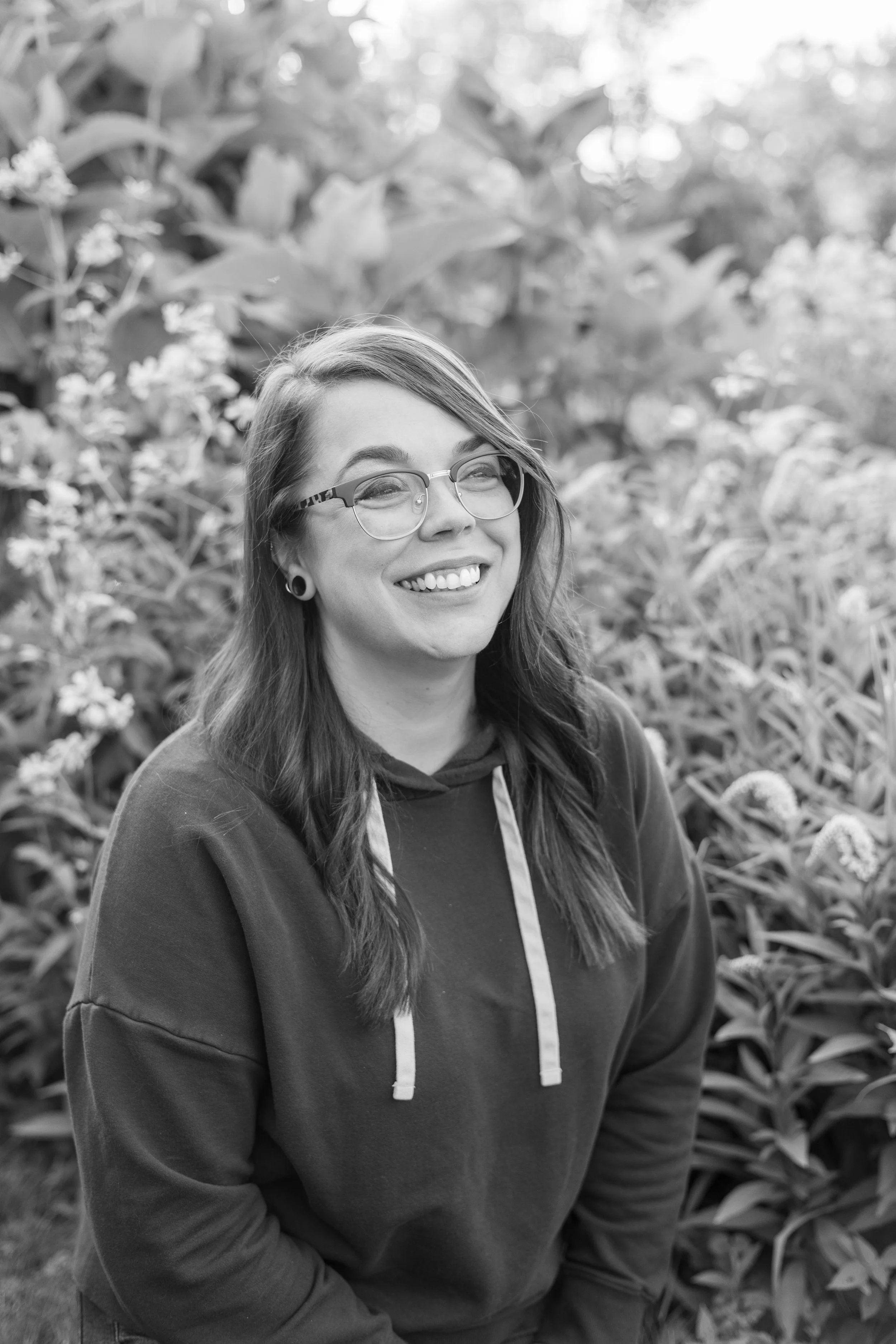 Photo of a woman smiling, sitting in front of tall grass and flowers
