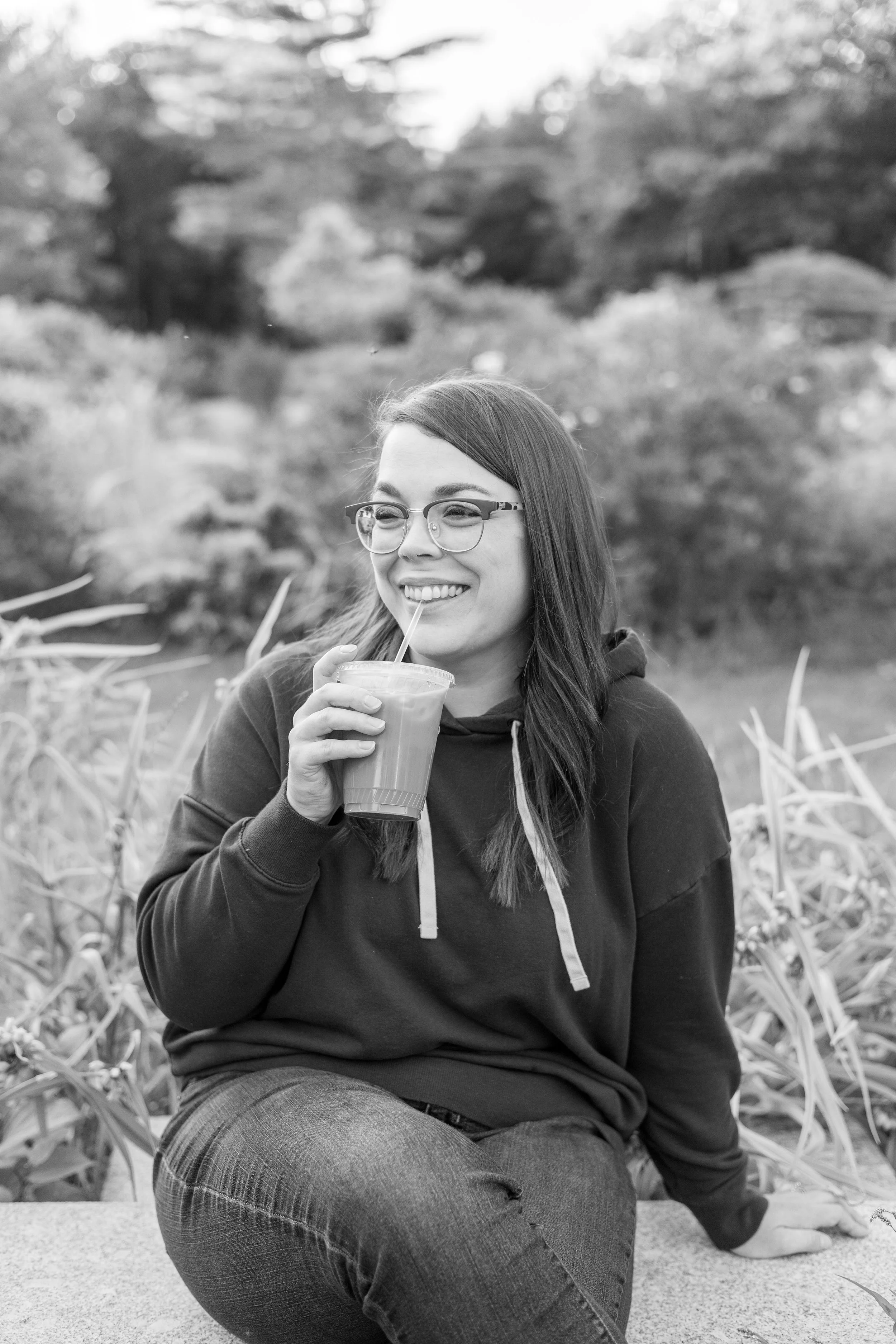 Photo of woman sitting in garden sipping iced coffee and smiling with her teeth