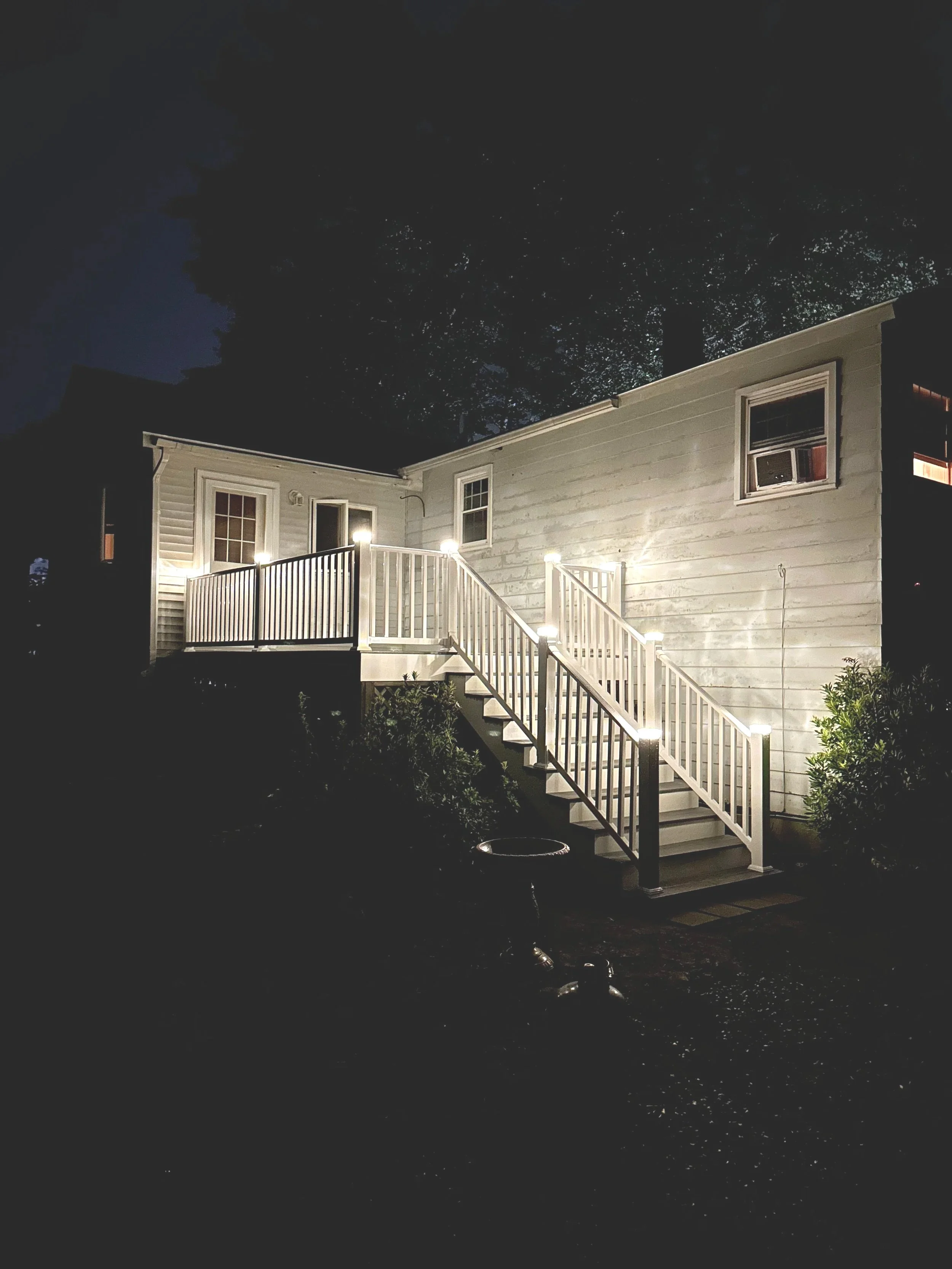 Exterior view of a house at night with a lit deck and staircase.