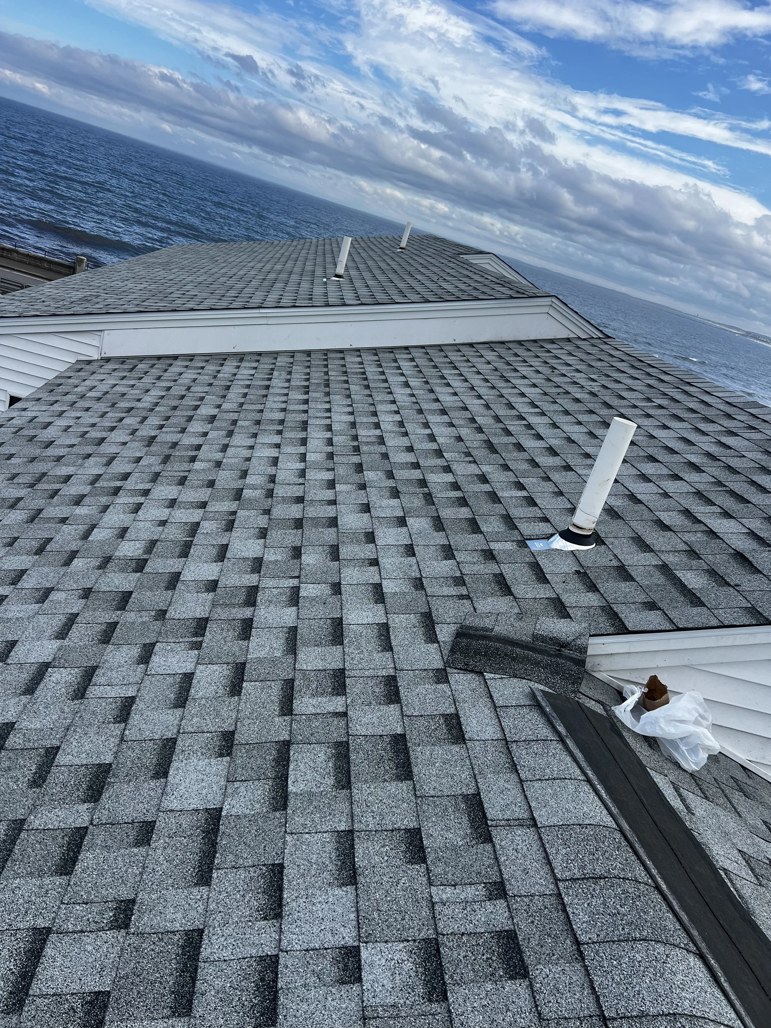 View of a gray shingled roof with vents overlooking a large body of water under a partly cloudy sky.
