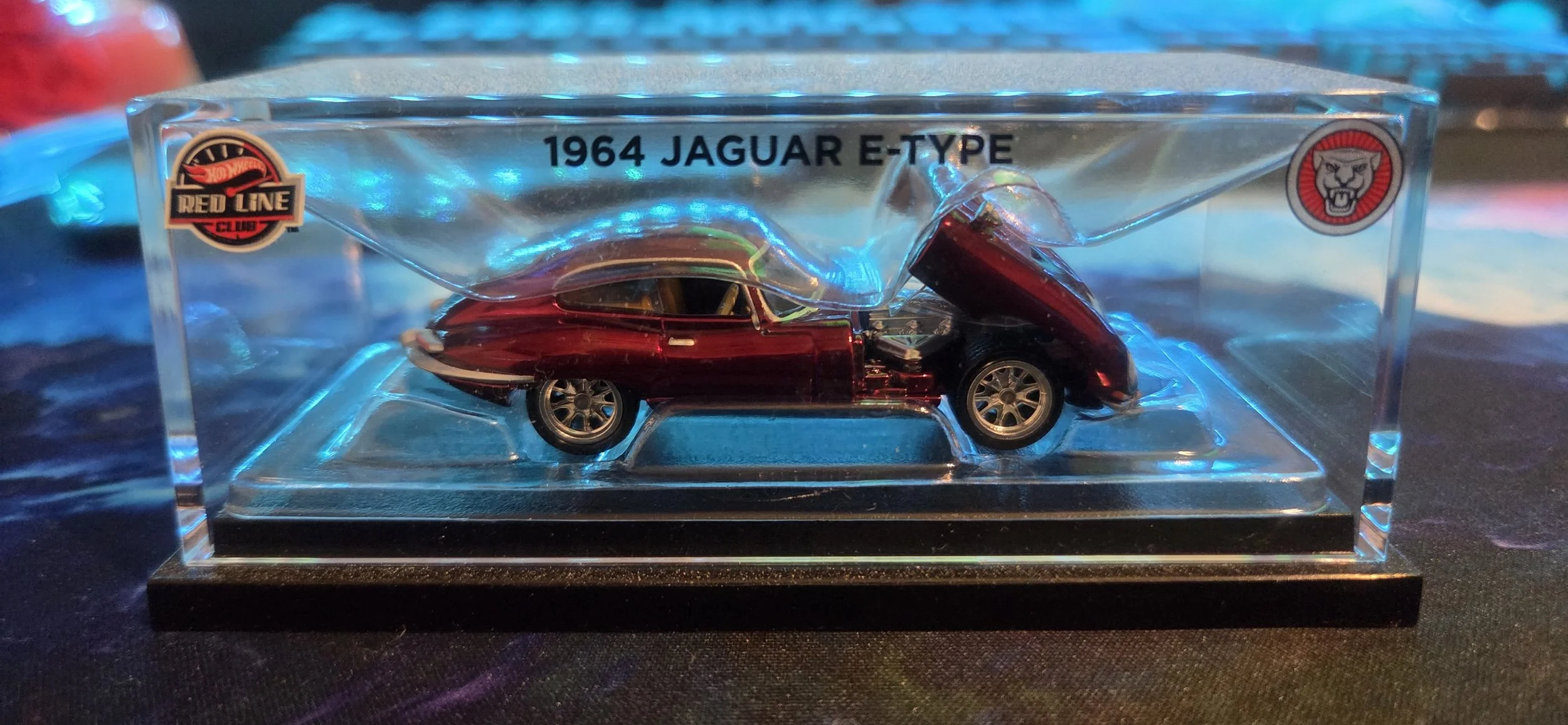 Miniature model of a 1964 Jaguar E-Type car in a clear display case with logos and labels.