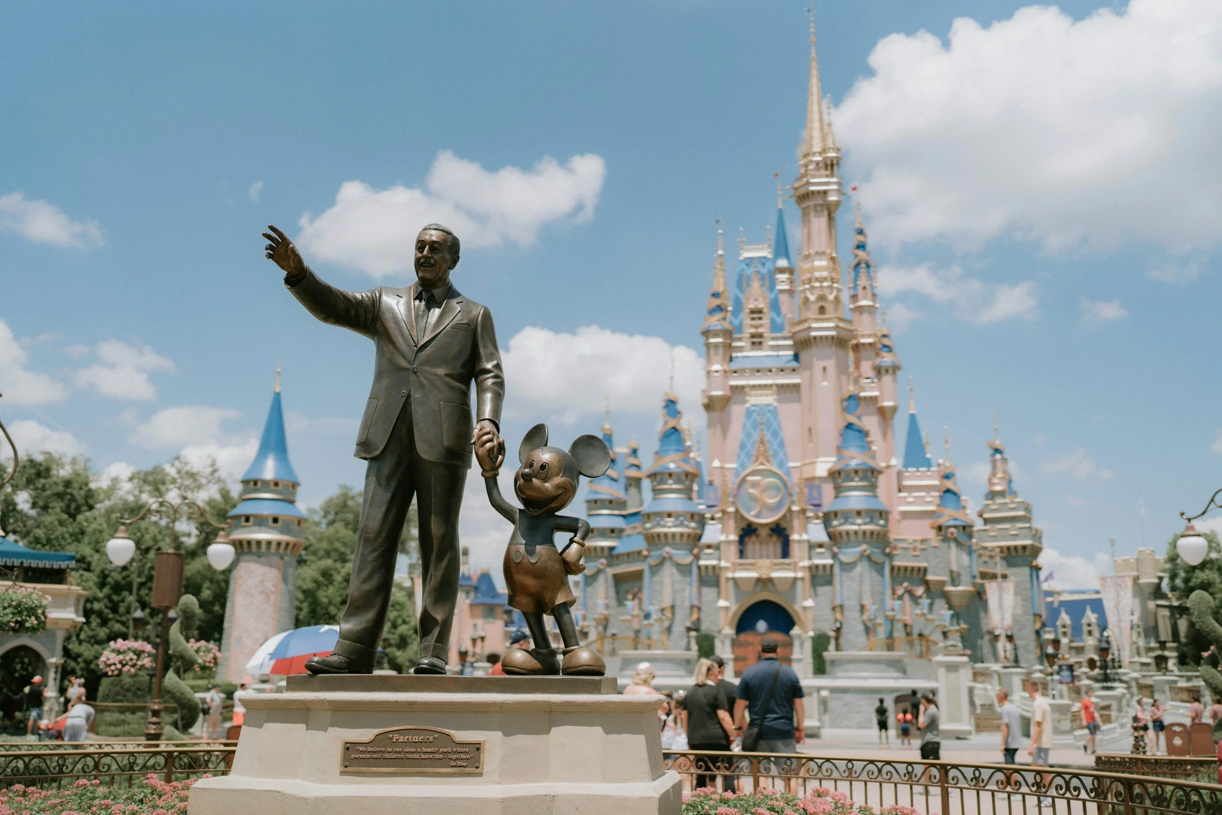 Statue of Walt Disney holding Mickey Mouse's hand in front of Sleeping Beauty Castle at Disneyland.