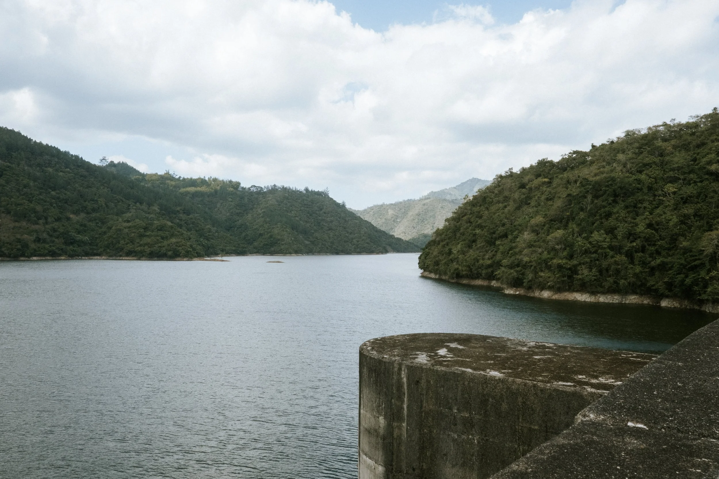 Embalse rodeado de colinas verdes y cielo parcialmente nublado.