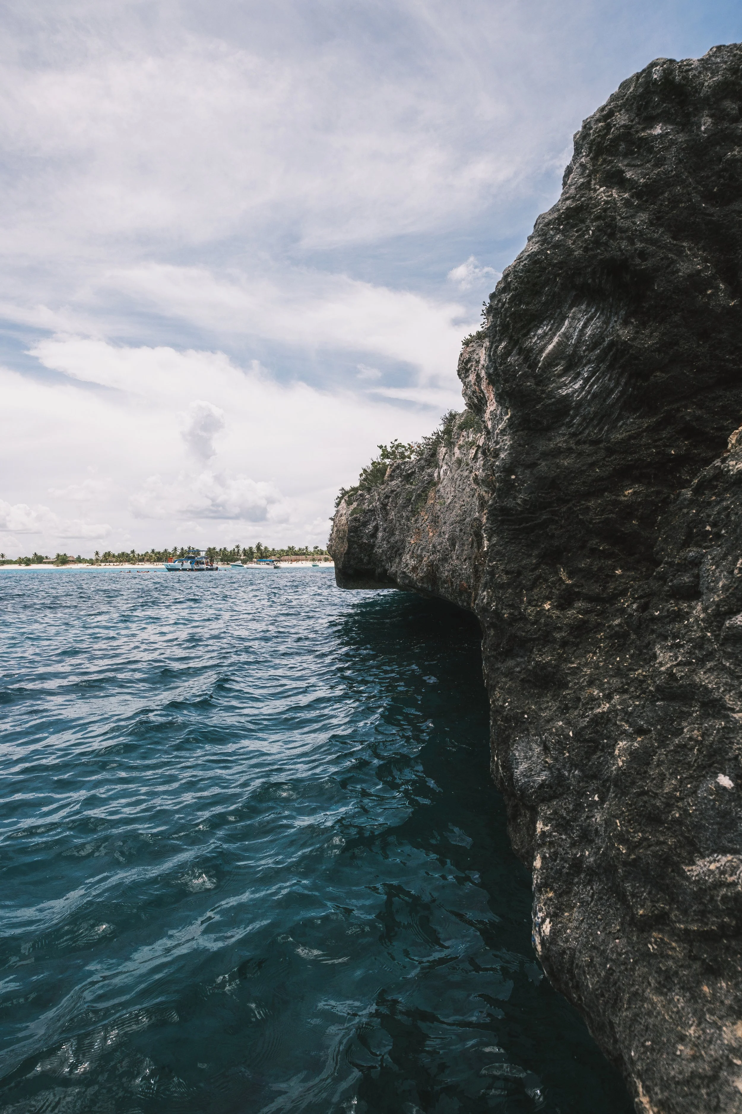 Costa rocosa junto al mar con agua azul, cielo nublado y vegetación en el fondo.