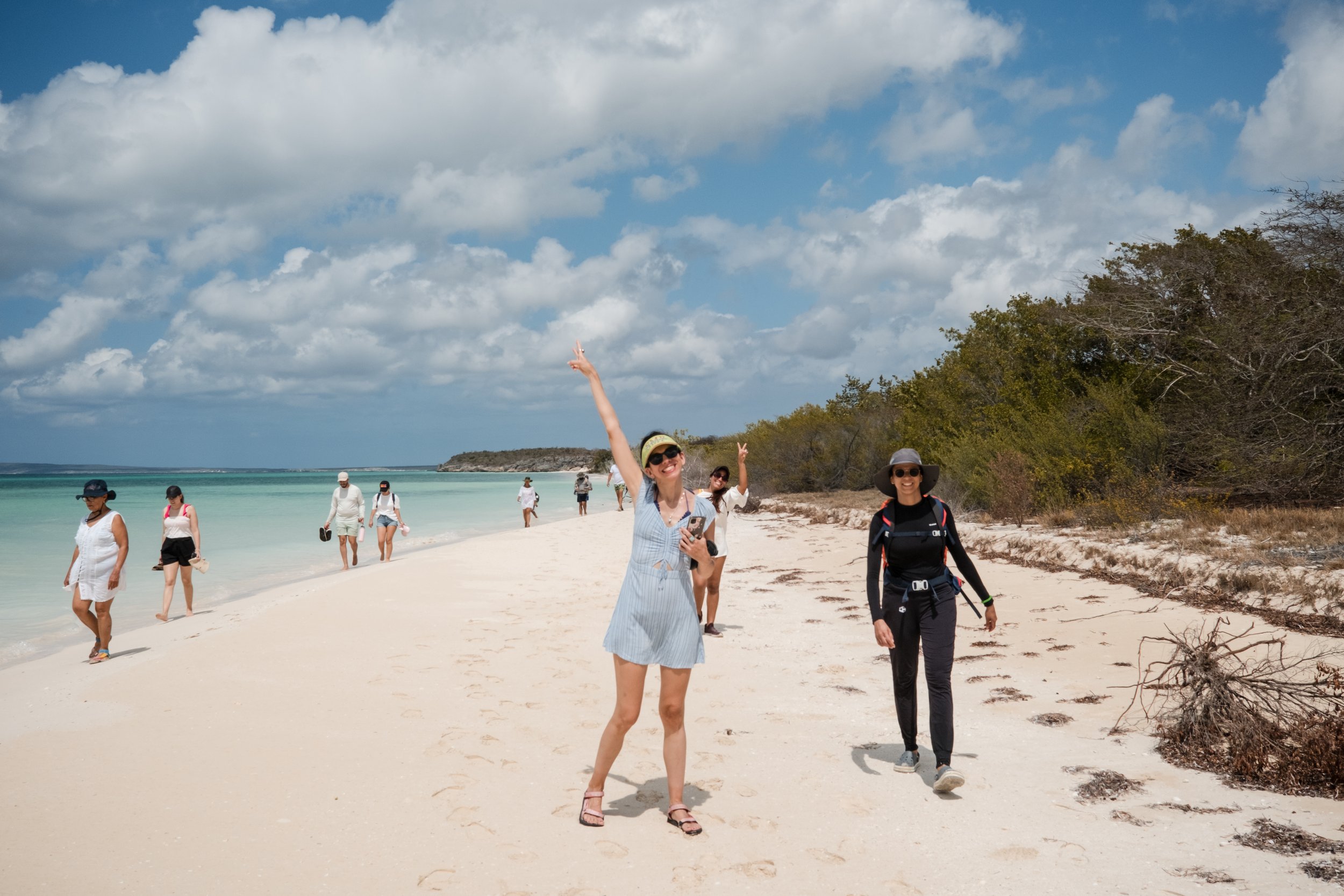 Personas caminando en una playa con cielo parcialmente nublado.