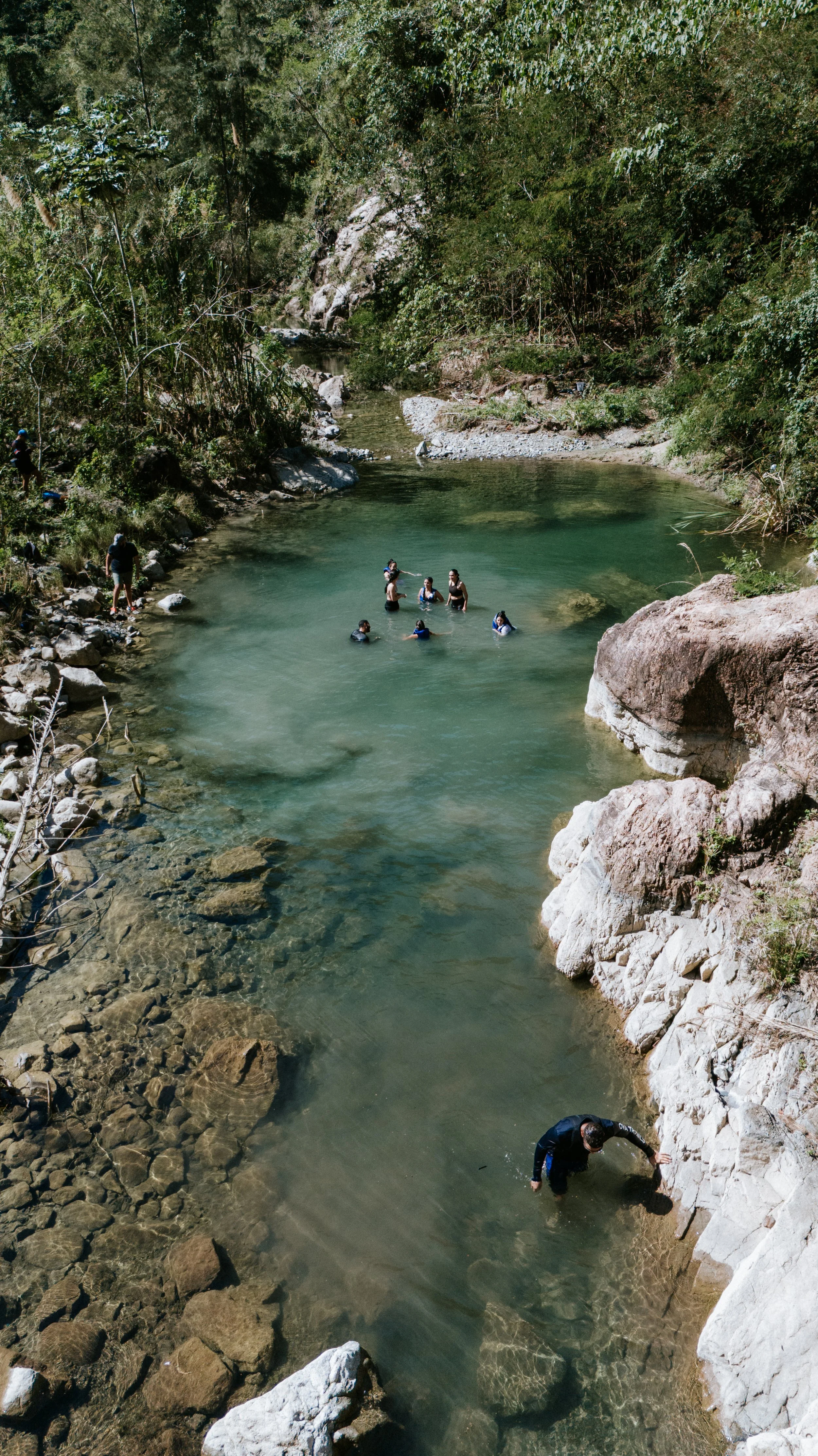 Personas nadando en un río rodeado de vegetación y rocas.