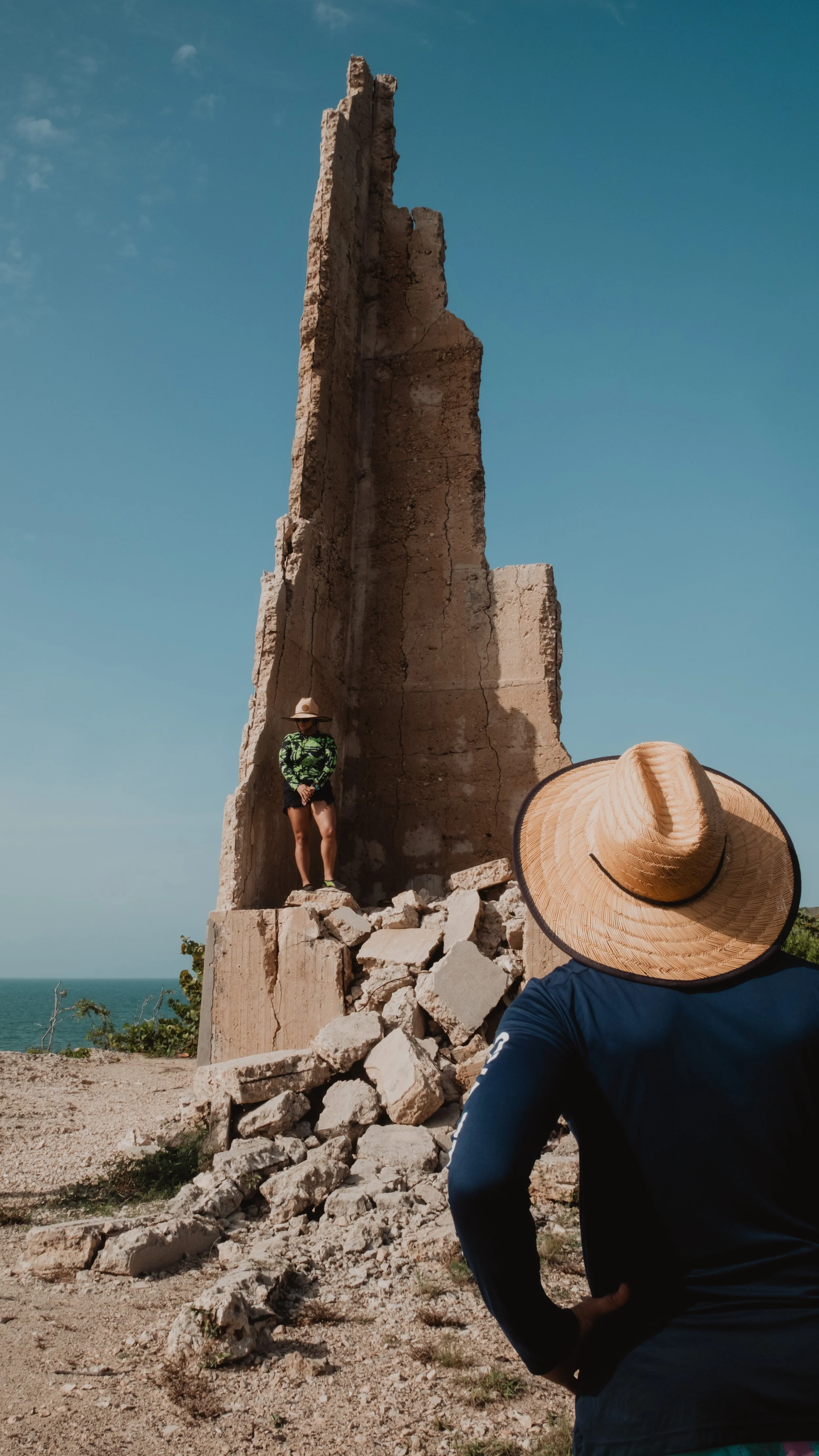 Persona con sombrero de paja de pie frente a una estructura de piedra al aire libre.
