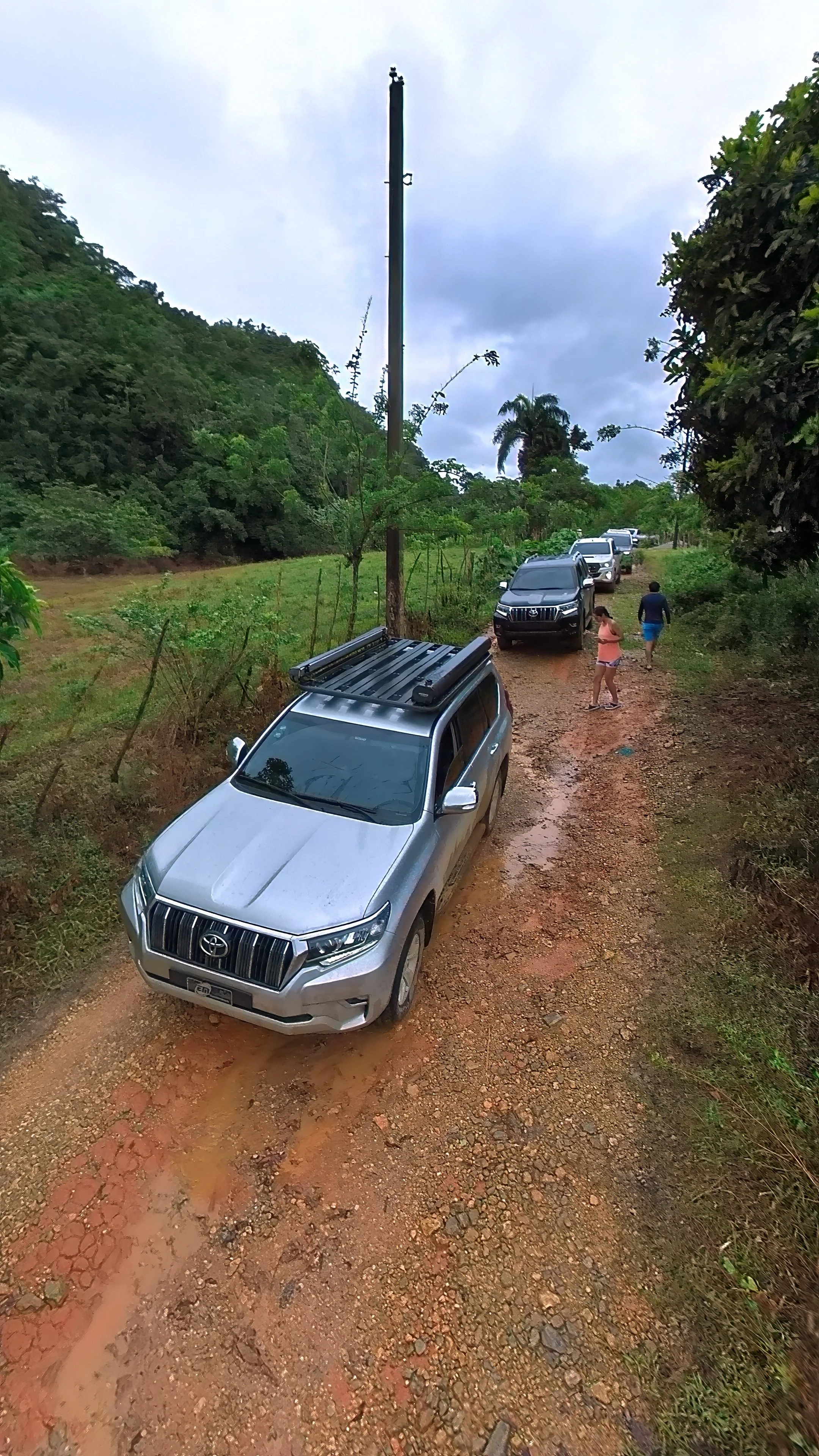 Carros todoterreno en un camino de tierra con vegetación alrededor y un poste de luz en el fondo.