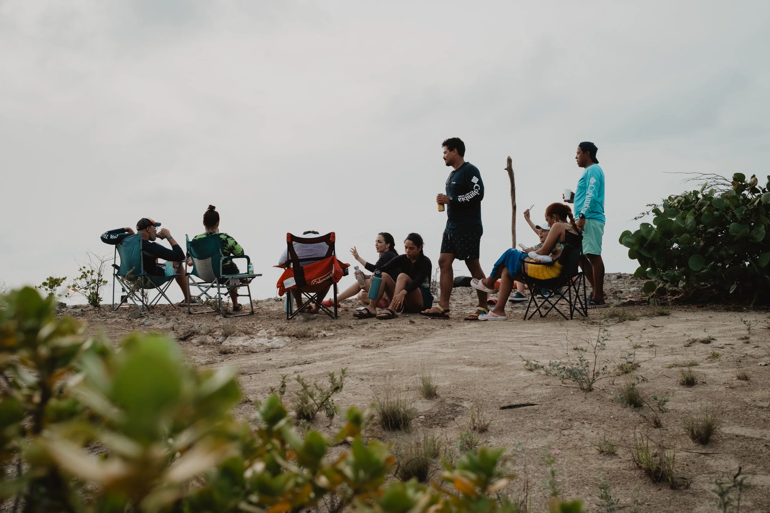 Grupo de personas sentadas en sillas de camping al aire libre en un ambiente natural.