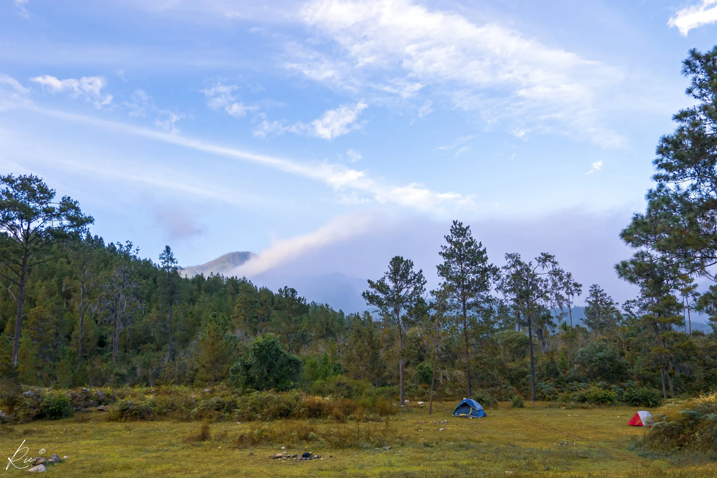 Paisaje montañoso con tiendas de campaña en un claro.
