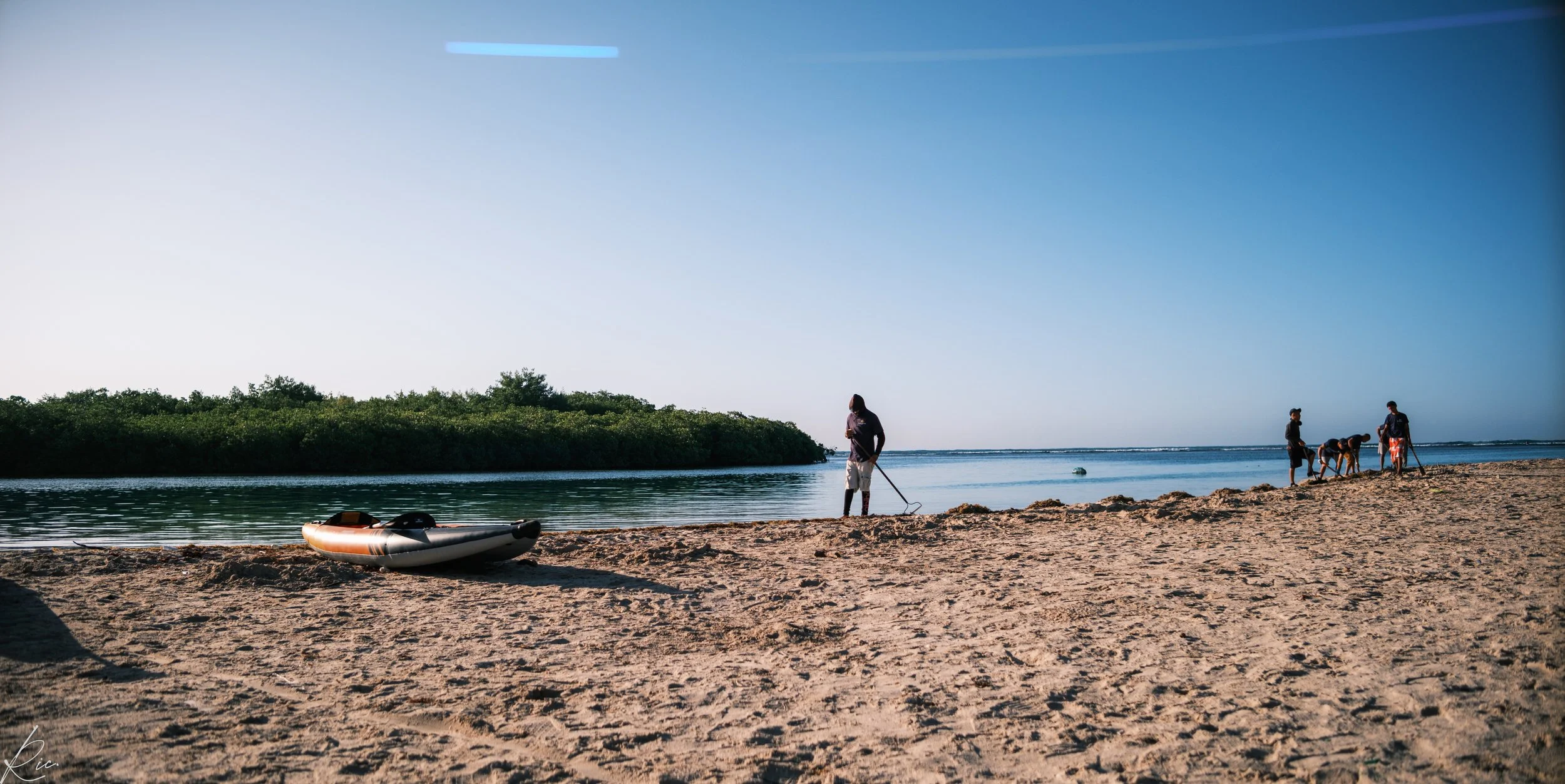 Playa con personas y kayak, vegetación al fondo.