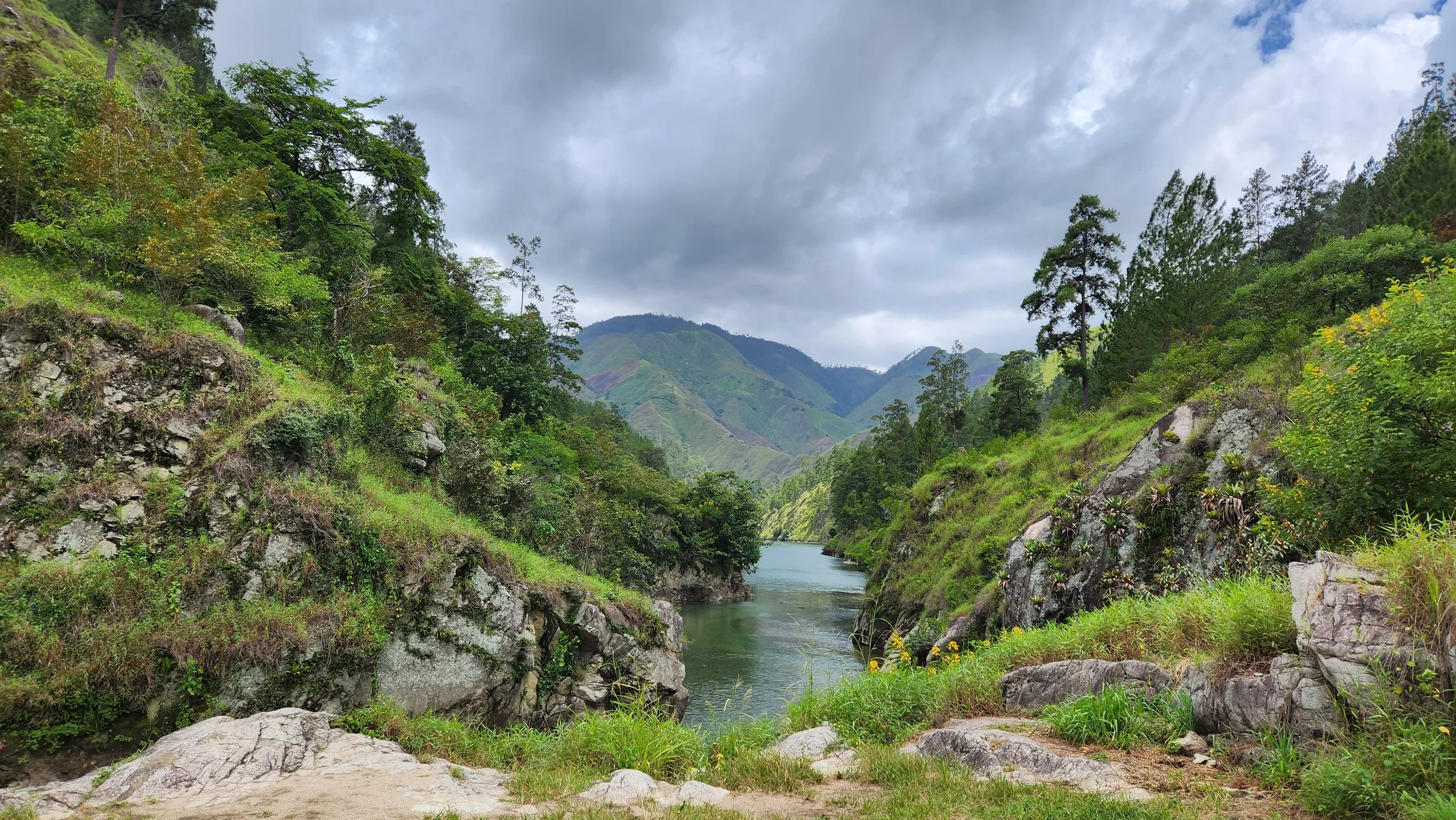 Paisaje montañoso con un río rodeado de vegetación abundante y cielos nublados.