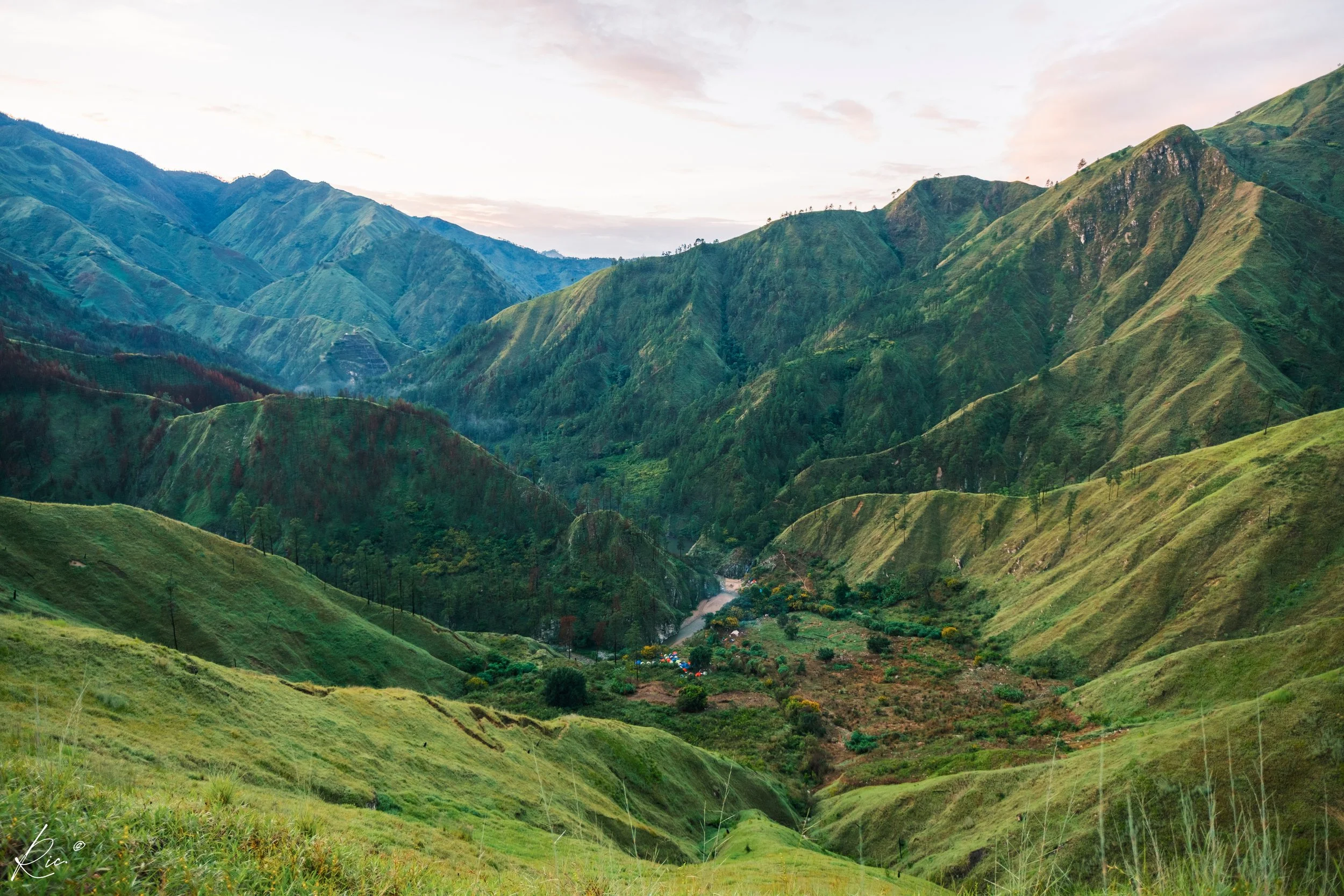 Paisaje montañoso con colinas verdes y un valle en el centro, bajo un cielo despejado.