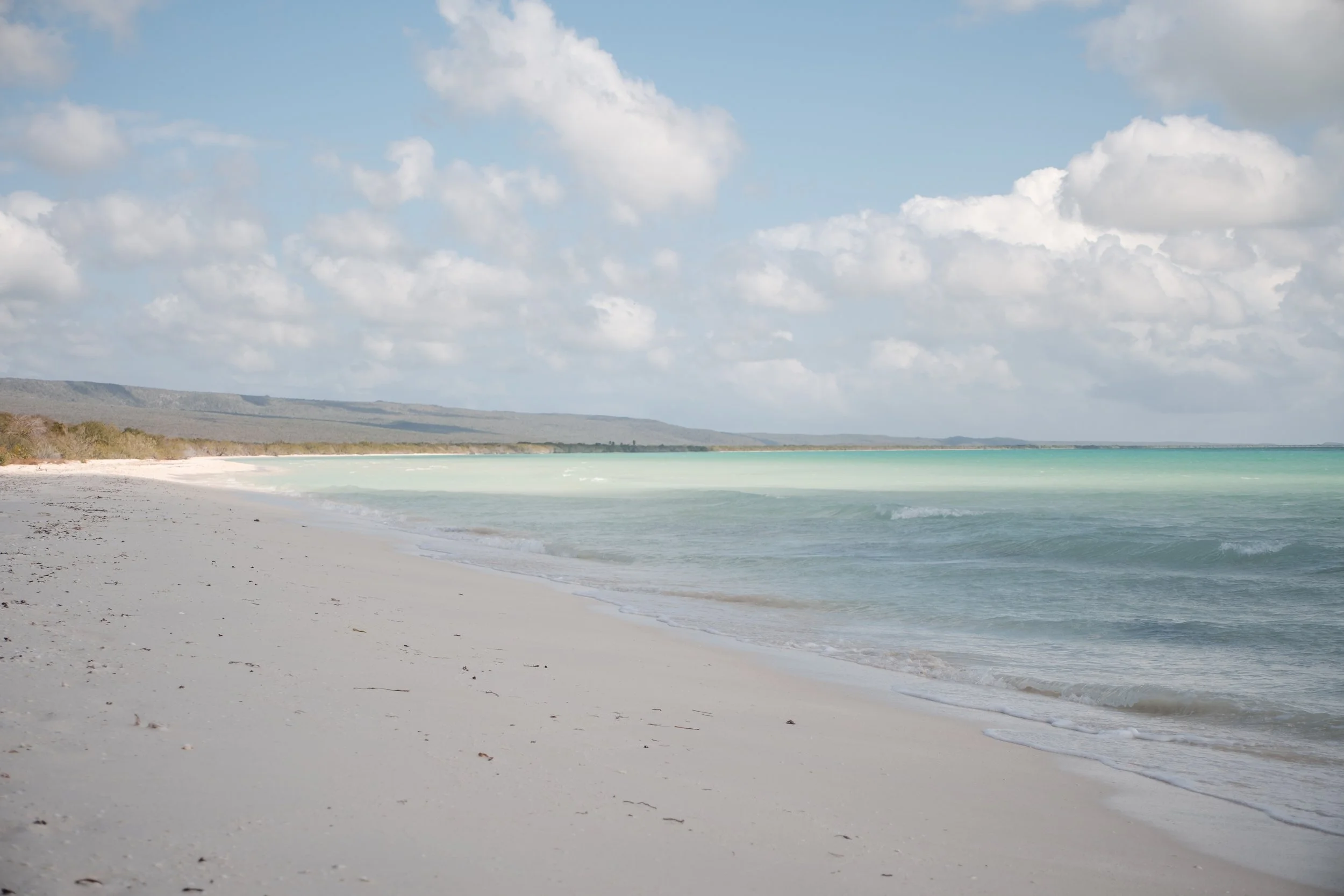 Playa con arena blanca, mar turquesa y cielo parcialmente nublado.