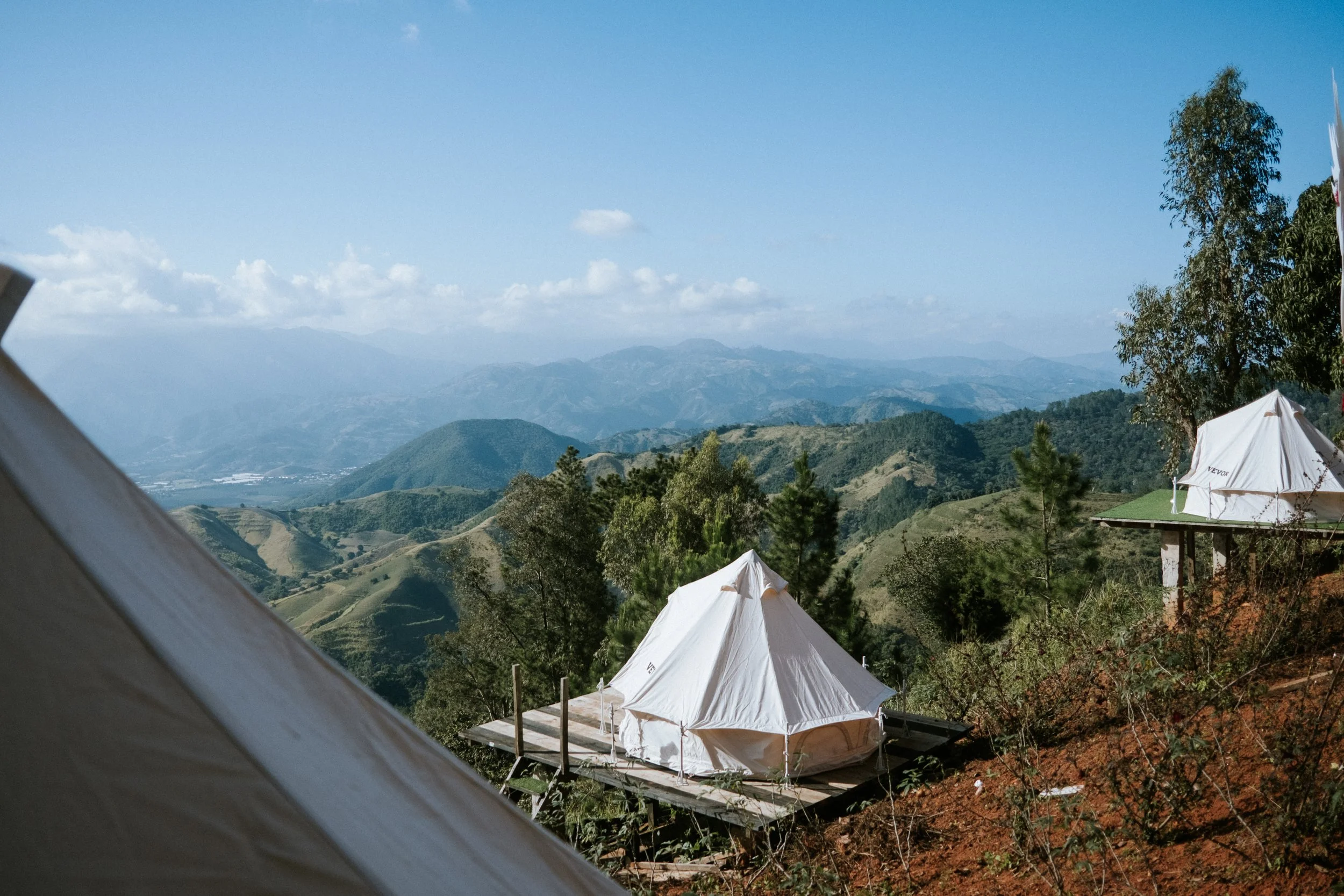Paisaje montañoso con tiendas de campaña de glamping en plataformas de madera, rodeadas de árboles y un cielo despejado.