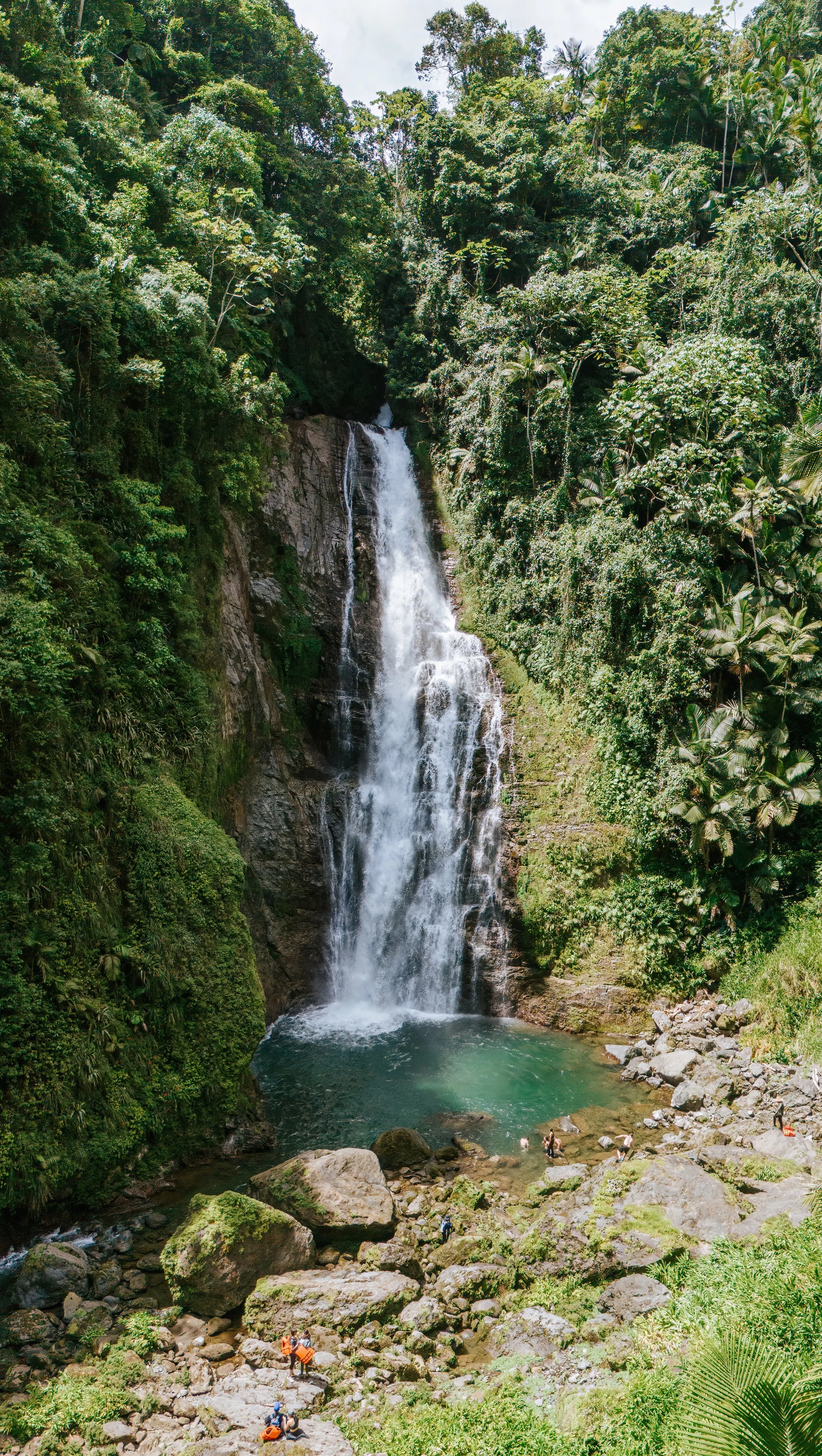 Cascada en un bosque tropical con personas en la base del salto de agua.