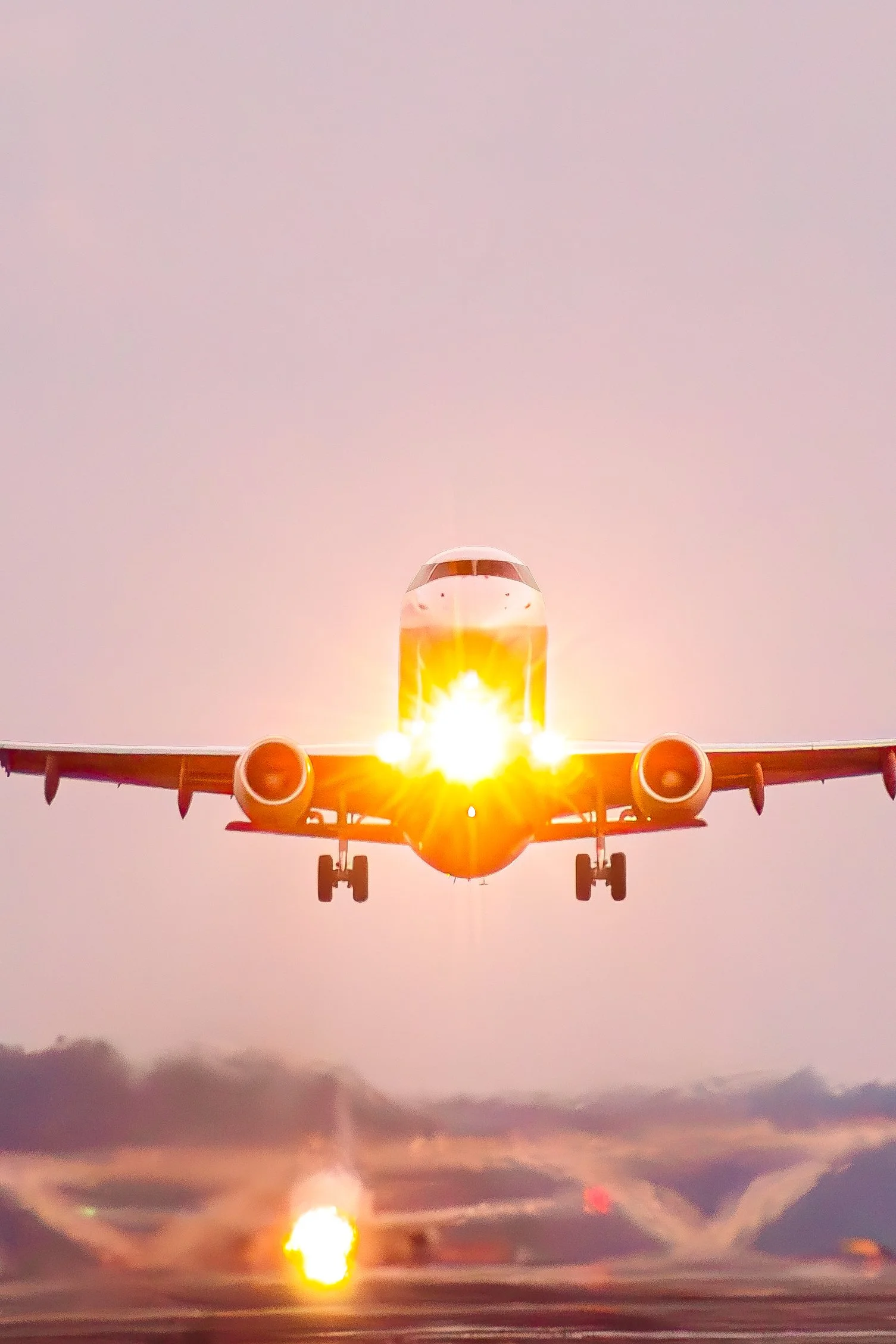Airplane taking off at sunrise with visible sun glare and cloudy sky.