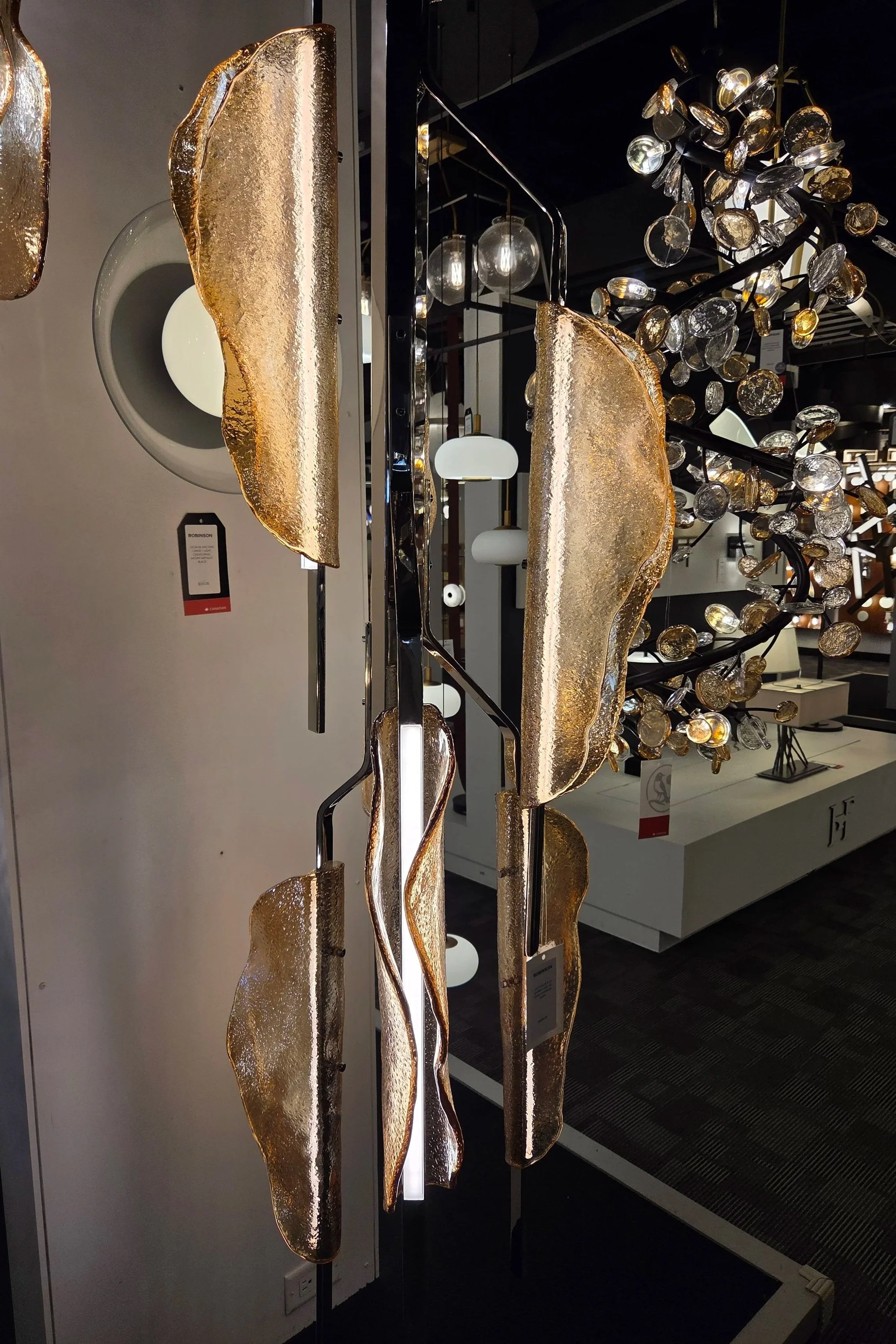 A modern chandelier with multiple glass orbs and gold-colored, textured, abstract sculptures hanging from black metal bars in a furniture or lighting store.