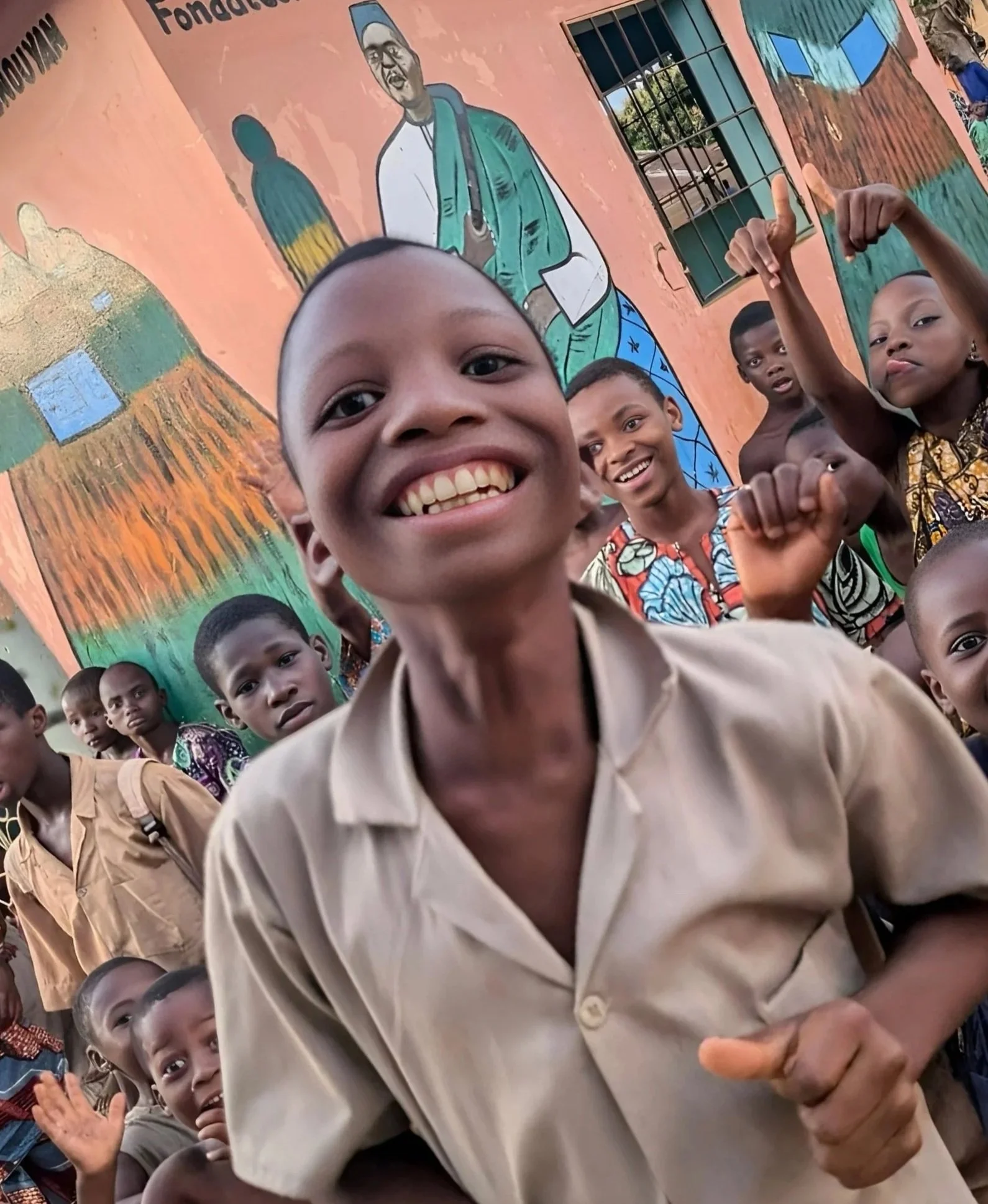 Smiling school children posing in front of colorful mural with a person playing a guitar painted on the wall.