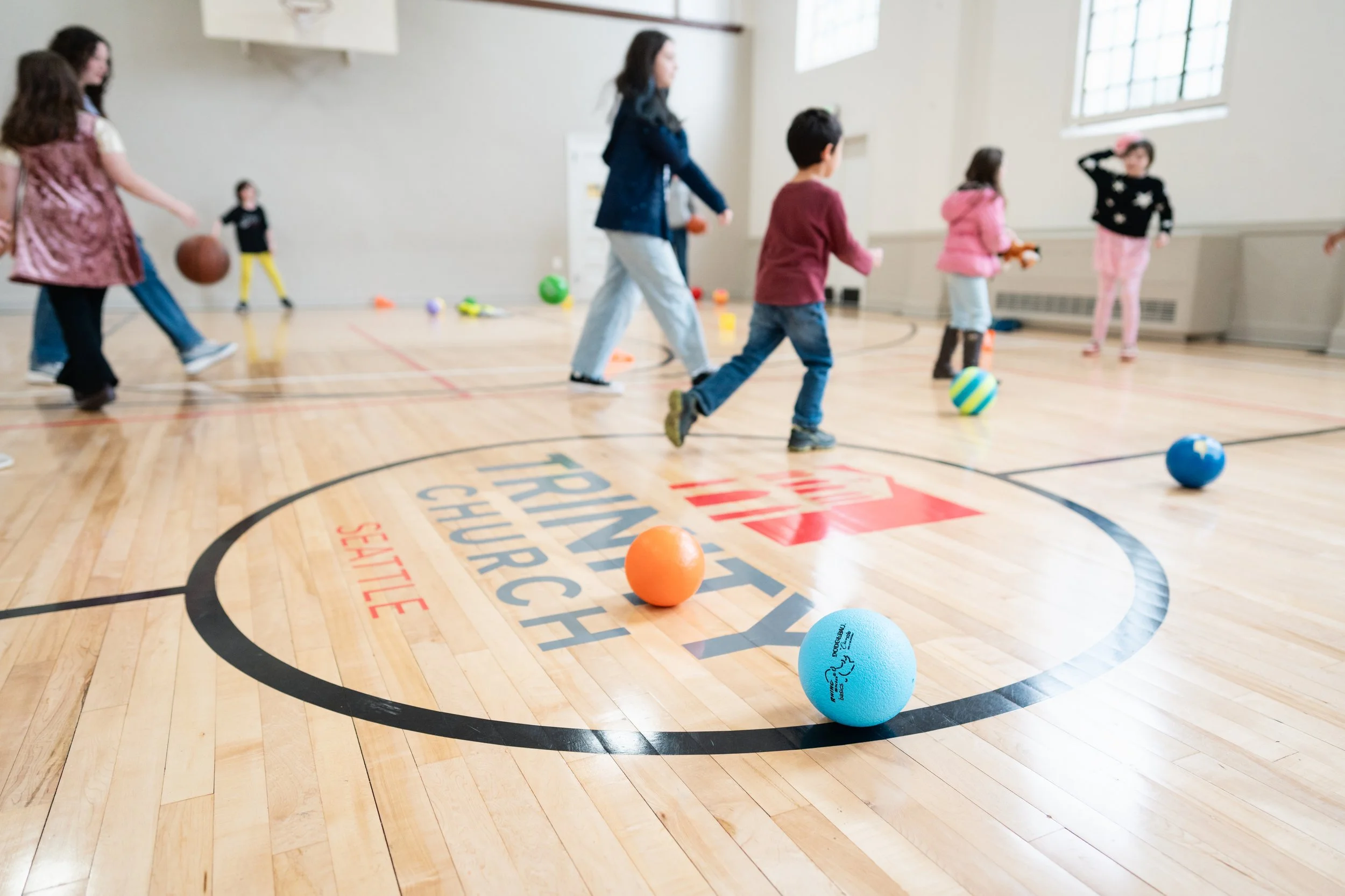 Children playing with balls and toys in a gymnasium.
