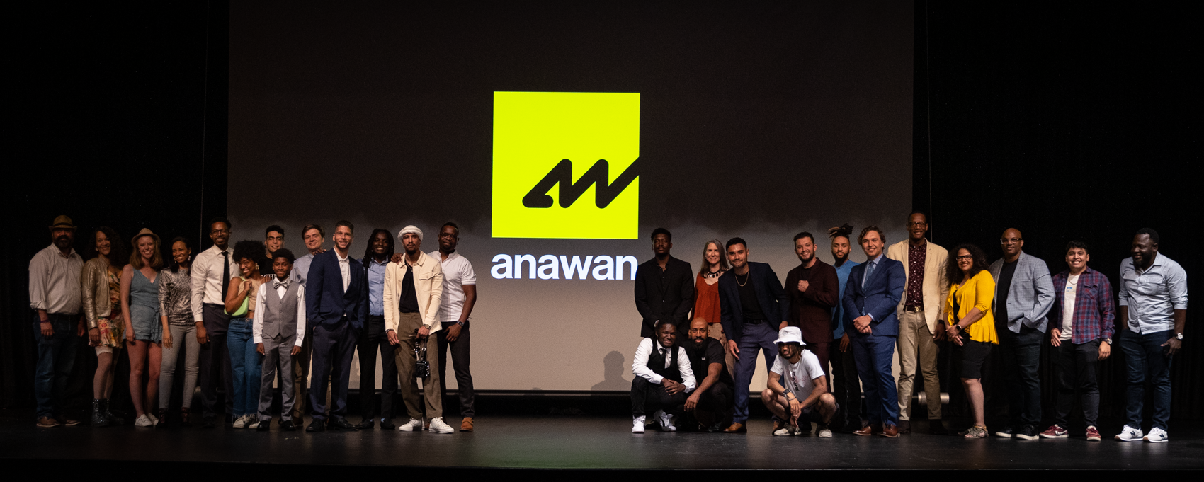 Group of diverse people on stage in front of a large screen displaying the logo of Anawan.