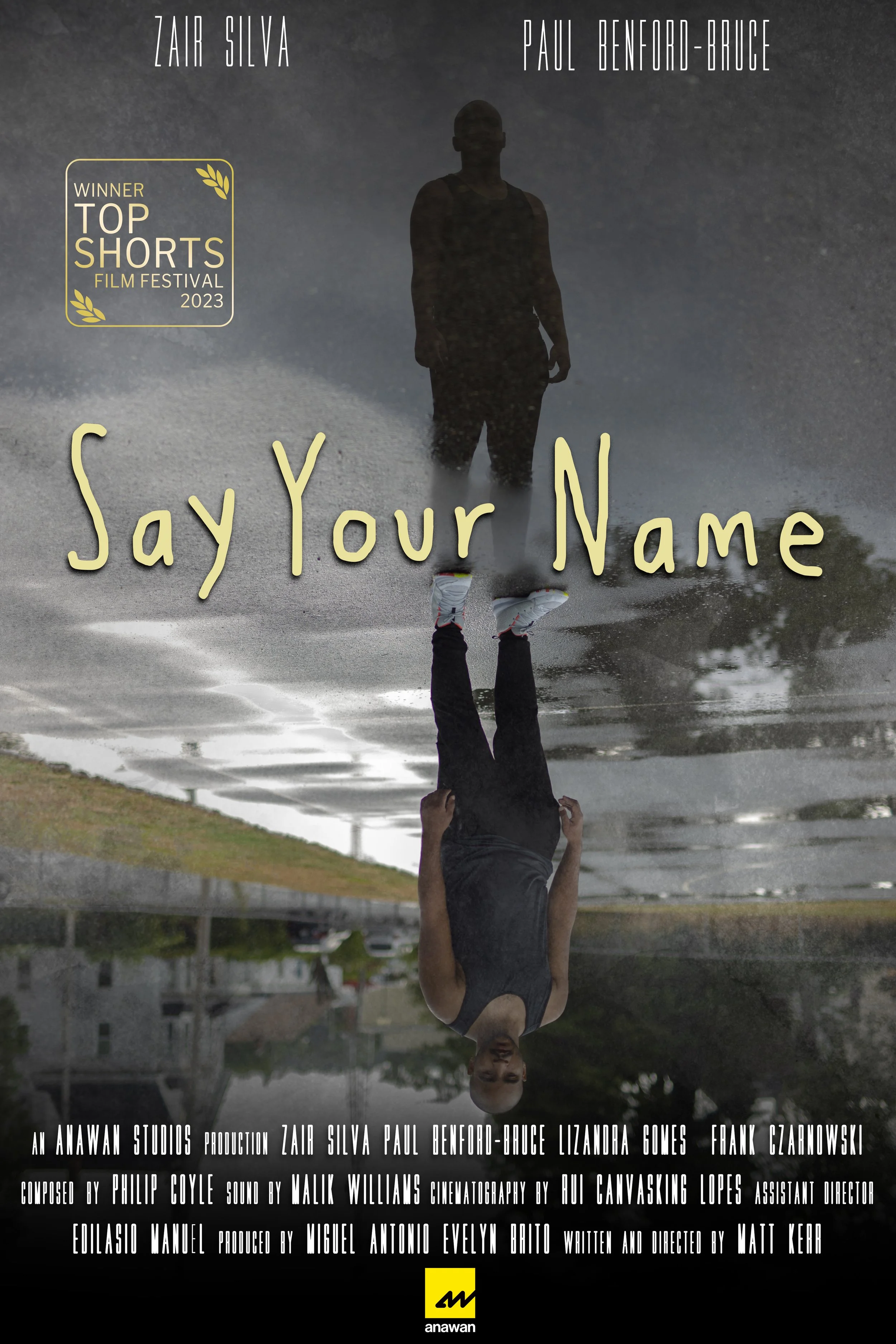 A movie poster for the short film titled 'Say Your Name', showing a silhouette of a person walking through a puddle of water with their reflection visible. The poster features the names Zair Silva and Paul Benford-Bruce, and includes awards for the f