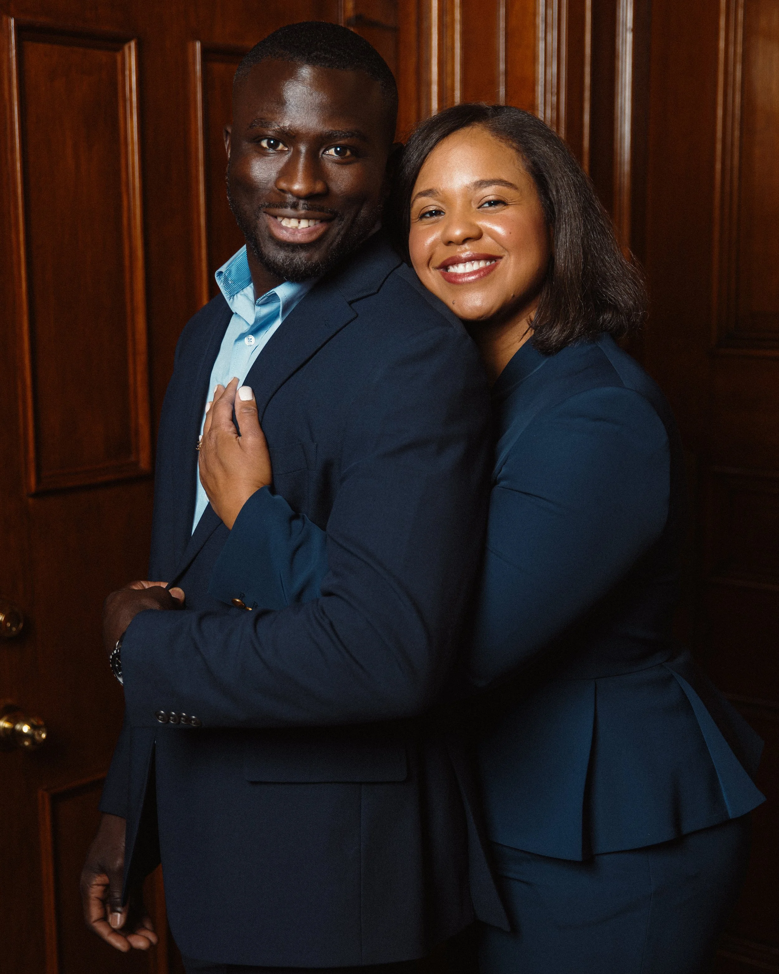 Francois & Iraimi Diatta of Empower Nutrition  in formal attire, standing close together indoors with wooden paneling in the background.