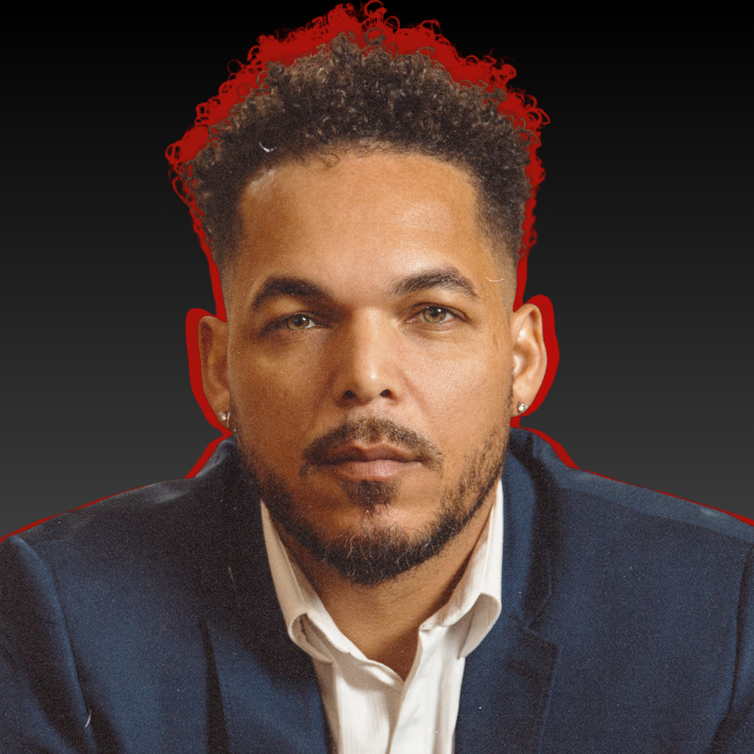 Salo Afonseca with curly hair and a beard, wearing a navy suit and white shirt, looking directly at the camera against a dark background with a red outline.