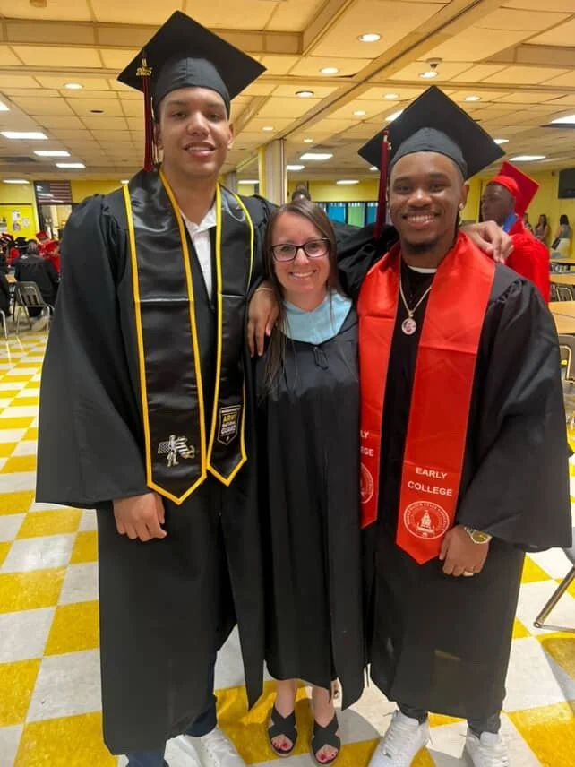 Two male graduates in caps and gowns standing with a woman in the middle at a graduation ceremony.