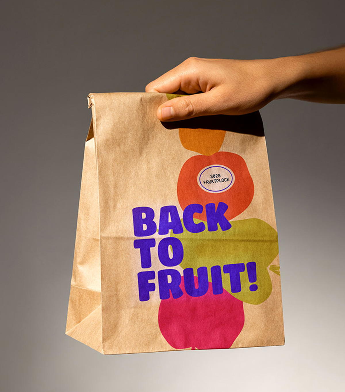 A paper bag with colorful fruit illustrations and the text 'Back to Fruit!' printed on it, held by a person's hand.