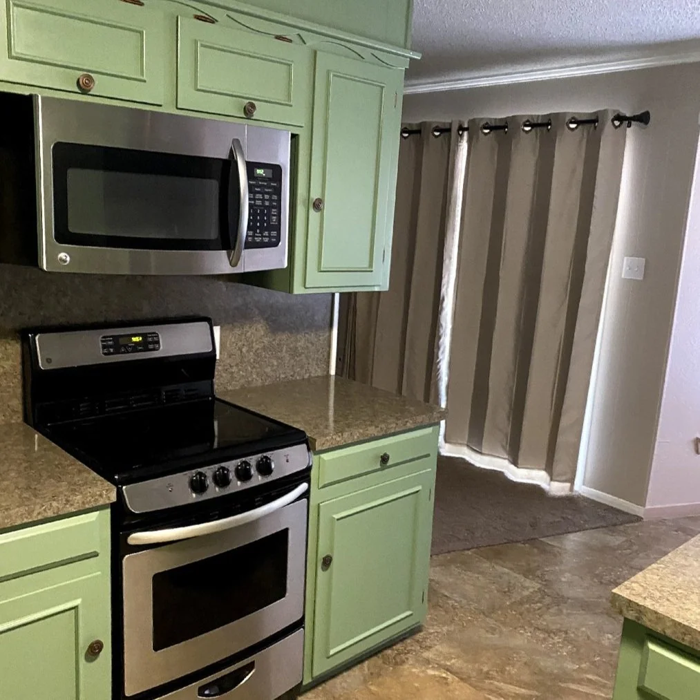 Kitchen with green cabinets, stainless steel oven, microwave, and brown curtains.