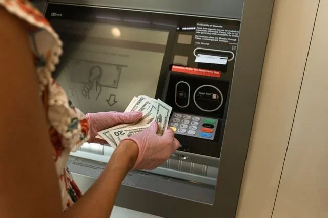 Person withdrawing cash from an ATM machine using pink gloves.