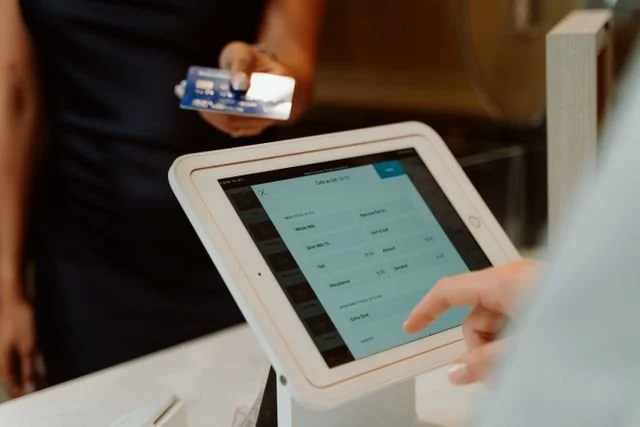Person using a tablet with a point-of-sale system, while another person holds a credit card nearby.