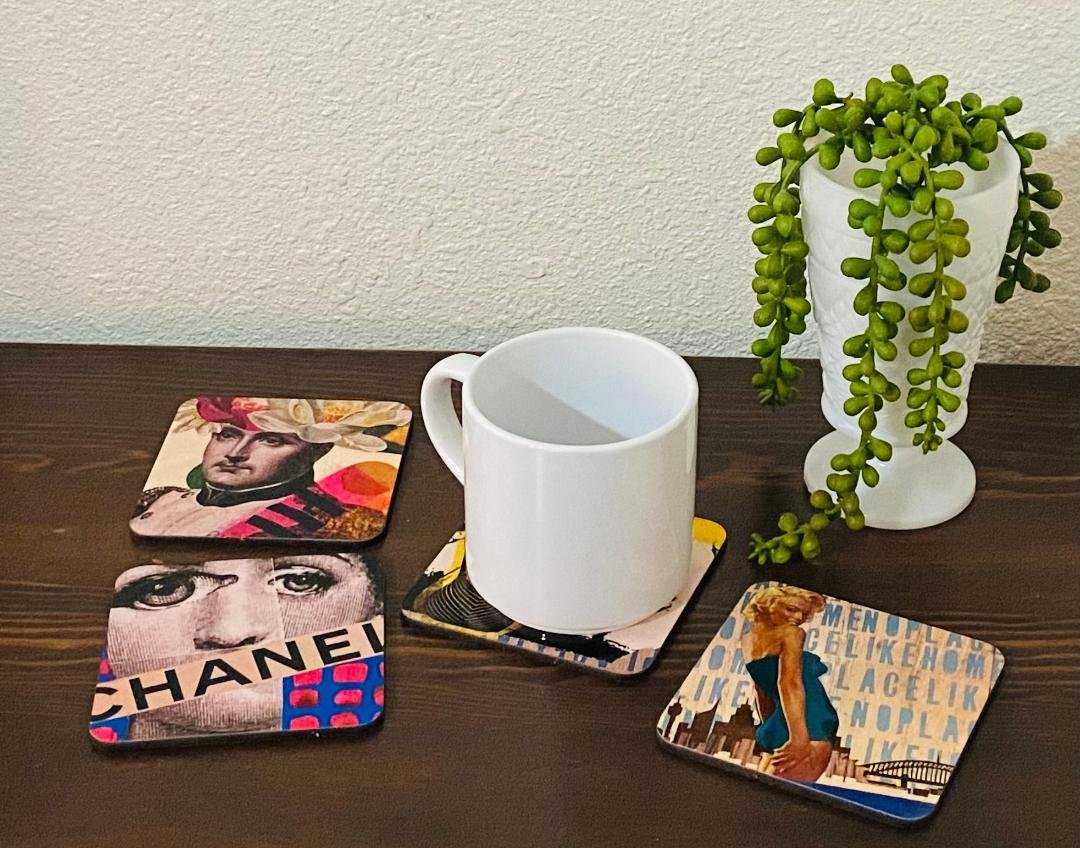A white mug on a wooden table surrounded by decorative coasters with artistic designs, and a white vase holding a trailing green plant.