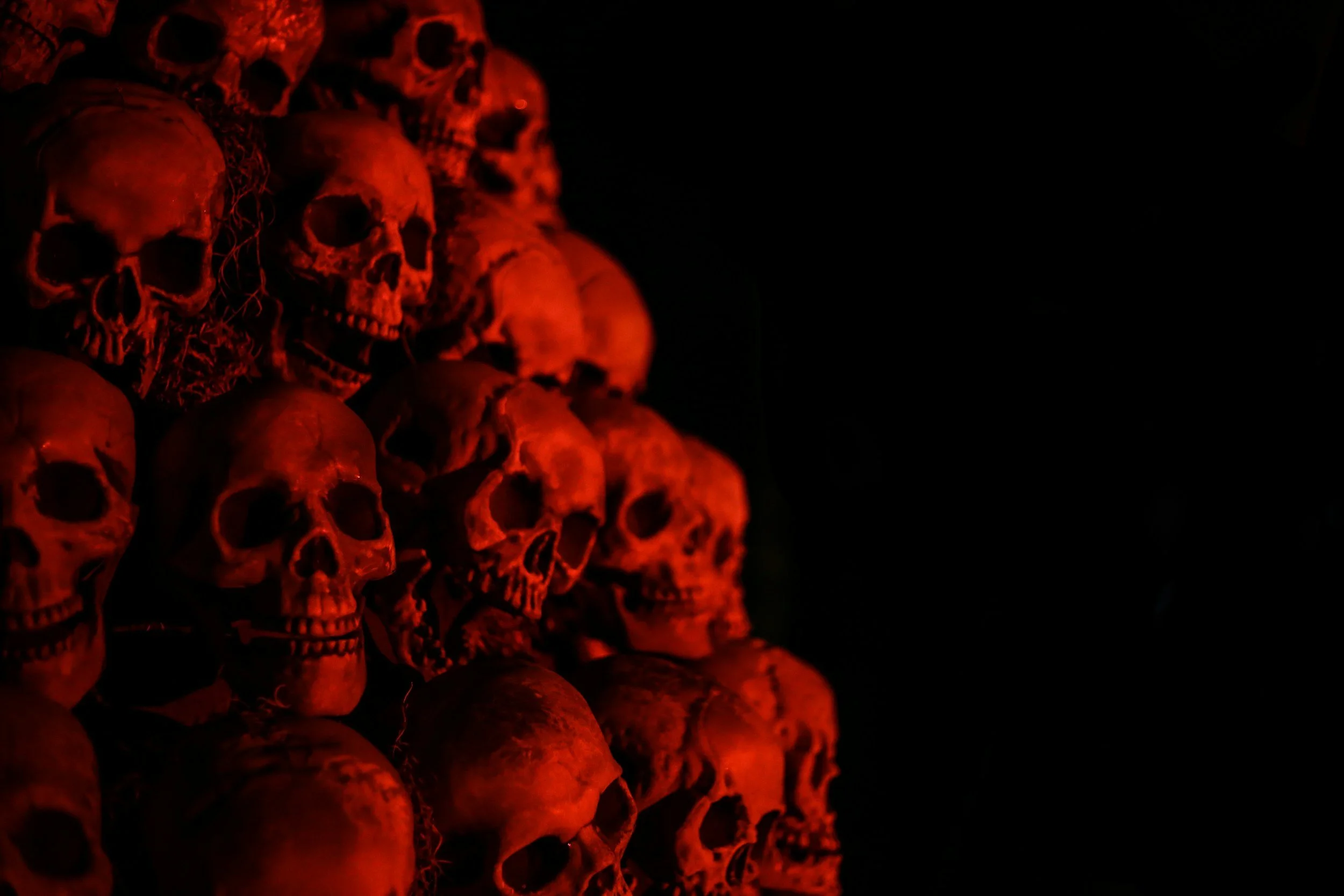 A stack of human skulls illuminated by red light on a dark background.