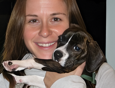 A woman smiling while holding a small brindle and white puppy.